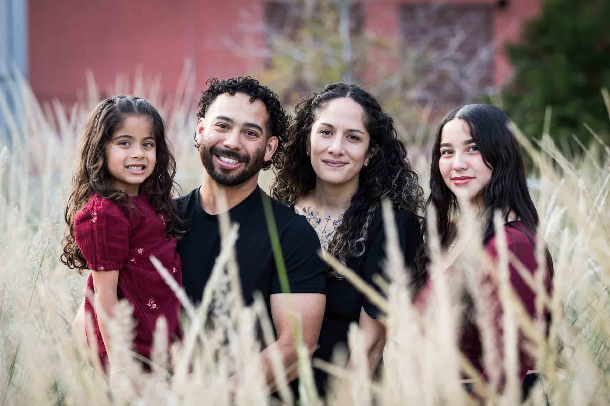 Family of two parents, teen girl, and little girl posed behind wheat-like bushes during a San Pedro Creek Park family portrait session