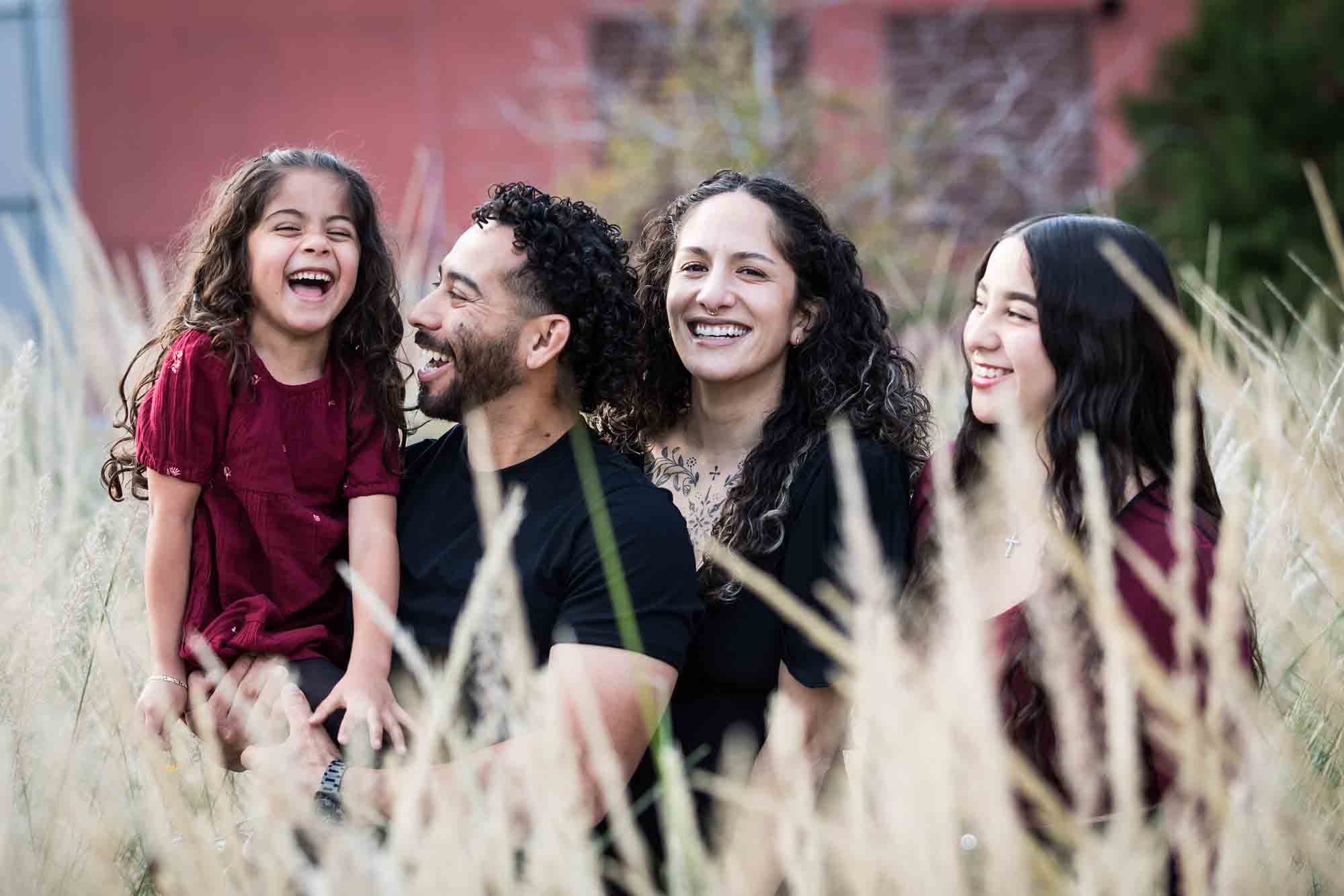 Family of two parents, teen girl, and little girl posed behind wheat-like bushes during a San Pedro Creek Park family portrait session