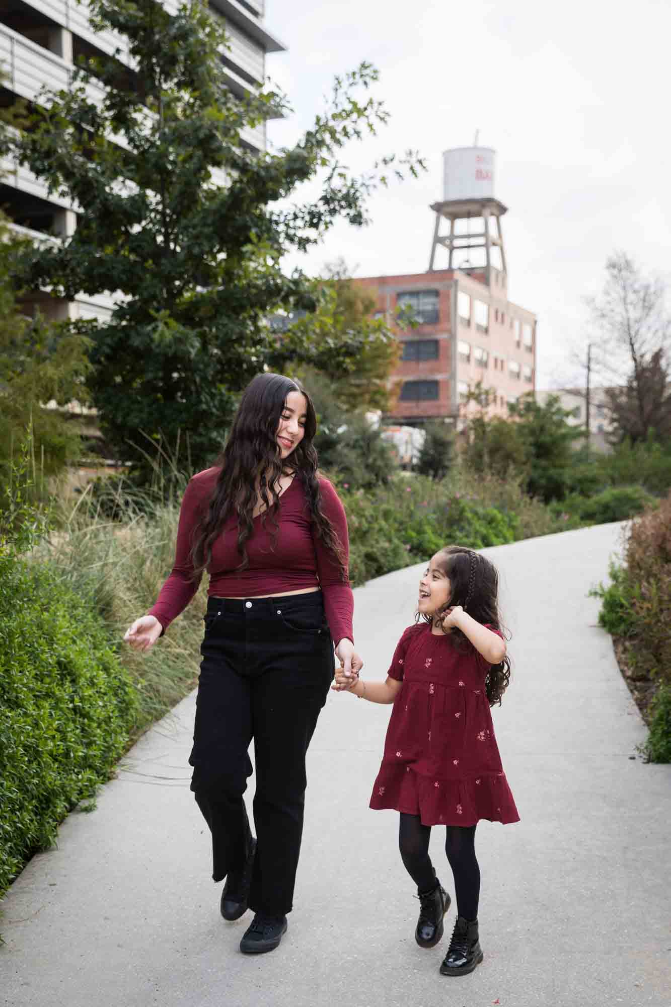 Older and younger sisters wearing maroon clothes walking on sidewalk during a San Pedro Creek Park family portrait session