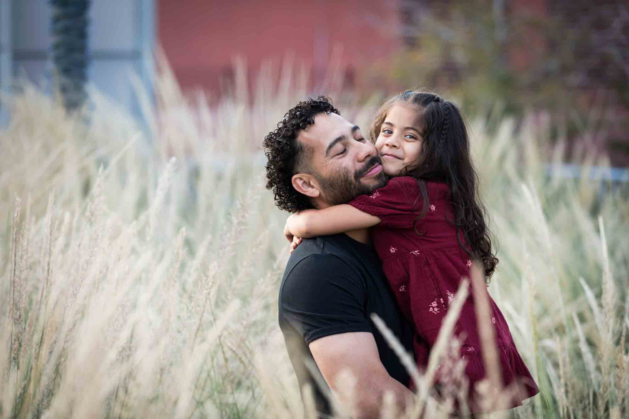 Father hugging little girl behind wheat-like bushes during a San Pedro Creek Park family portrait session