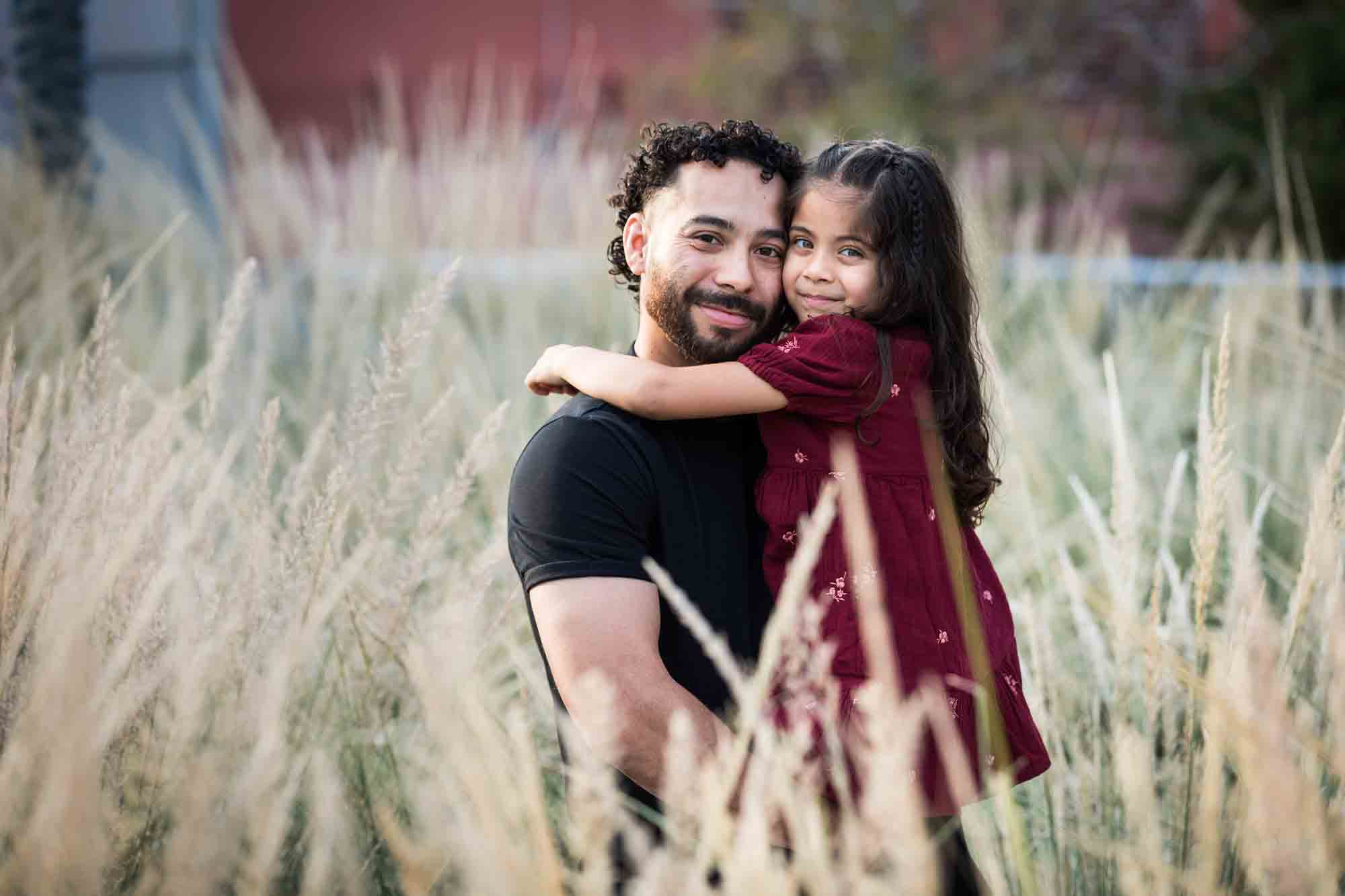 Father hugging little girl behind wheat-like bushes during a San Pedro Creek Park family portrait session