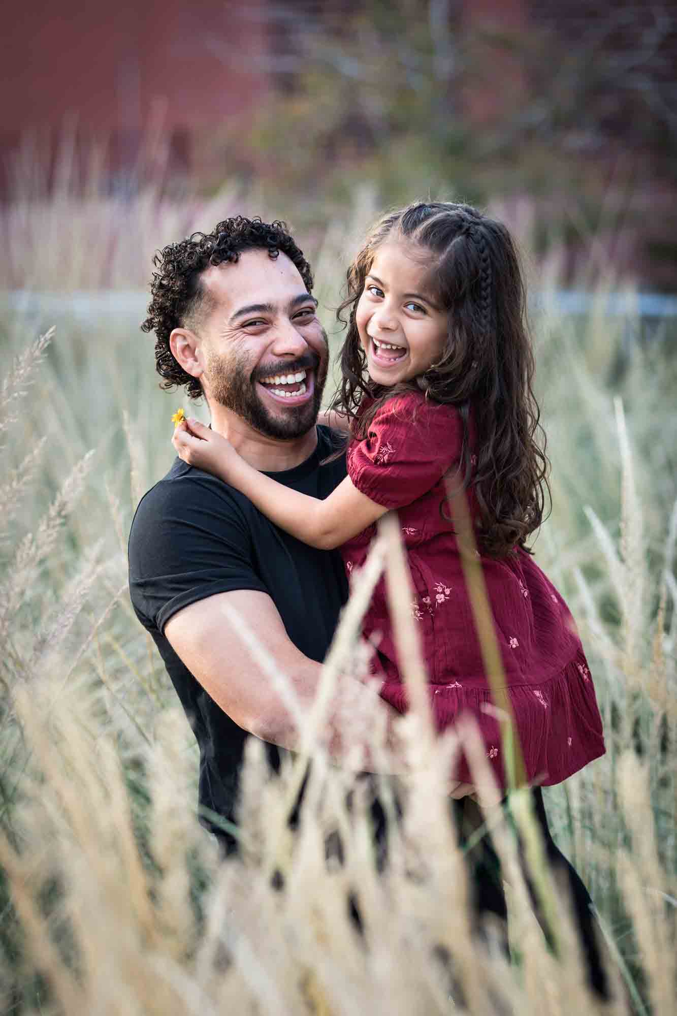 Father hugging little girl behind wheat-like bushes during a San Pedro Creek Park family portrait session