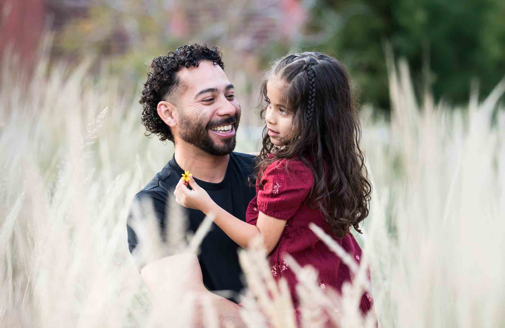 Father hugging little girl behind wheat-like bushes during a San Pedro Creek Park family portrait session