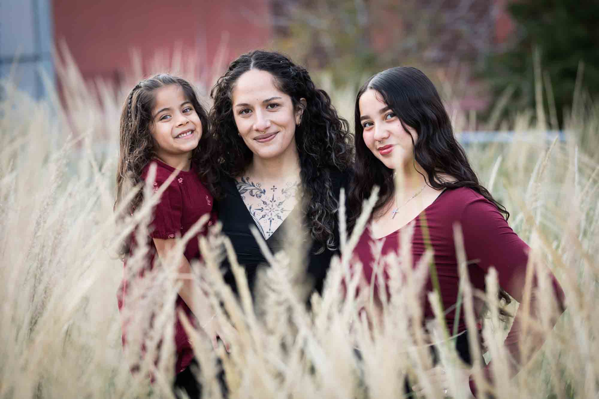 Mother, teen girl, and little girl posed behind wheat-like bushes during a San Pedro Creek Park family portrait session