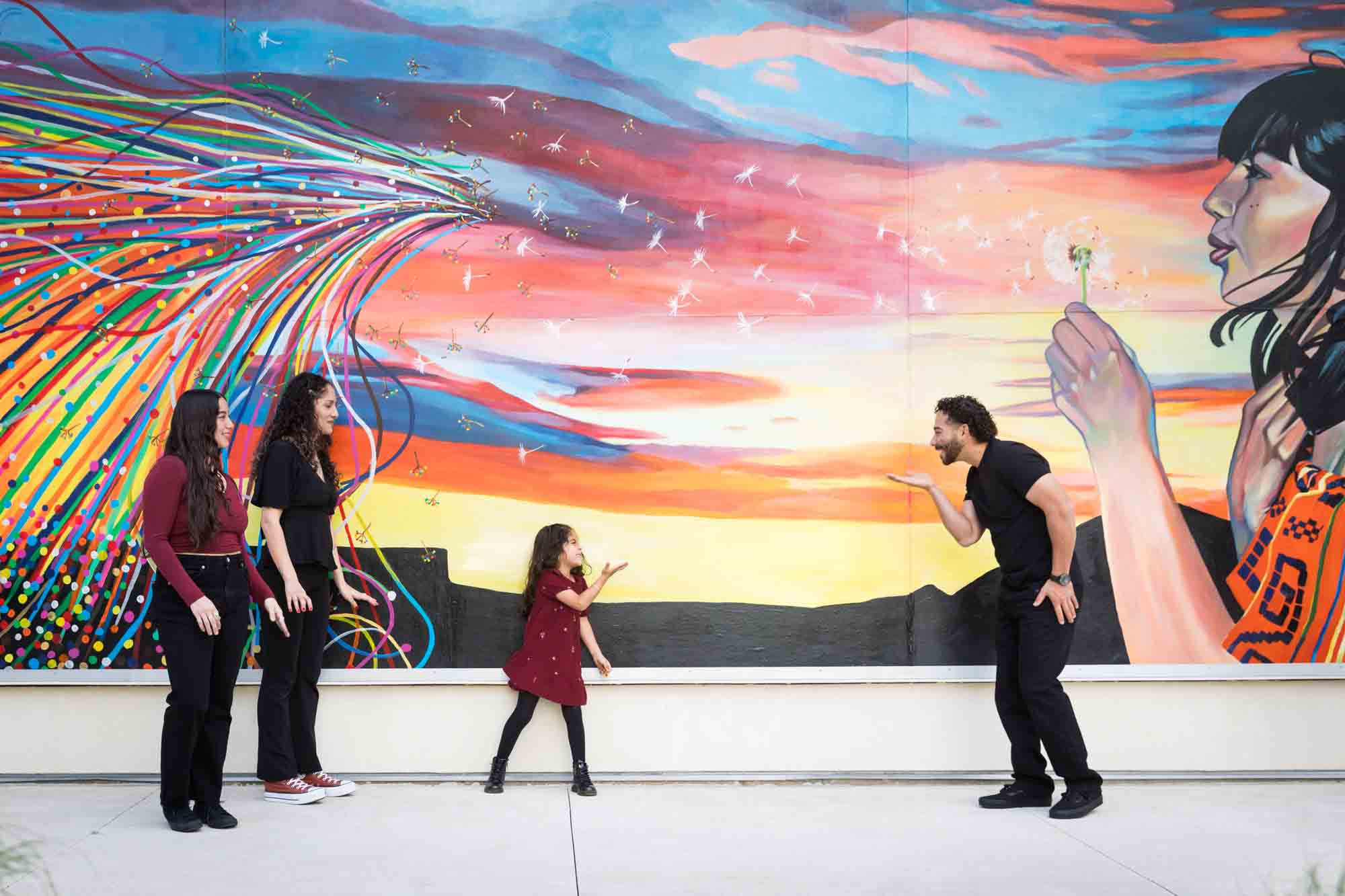 Family of two parents, teen girl and little girl playing in front of colorful mural by UTSA Data Sciences building