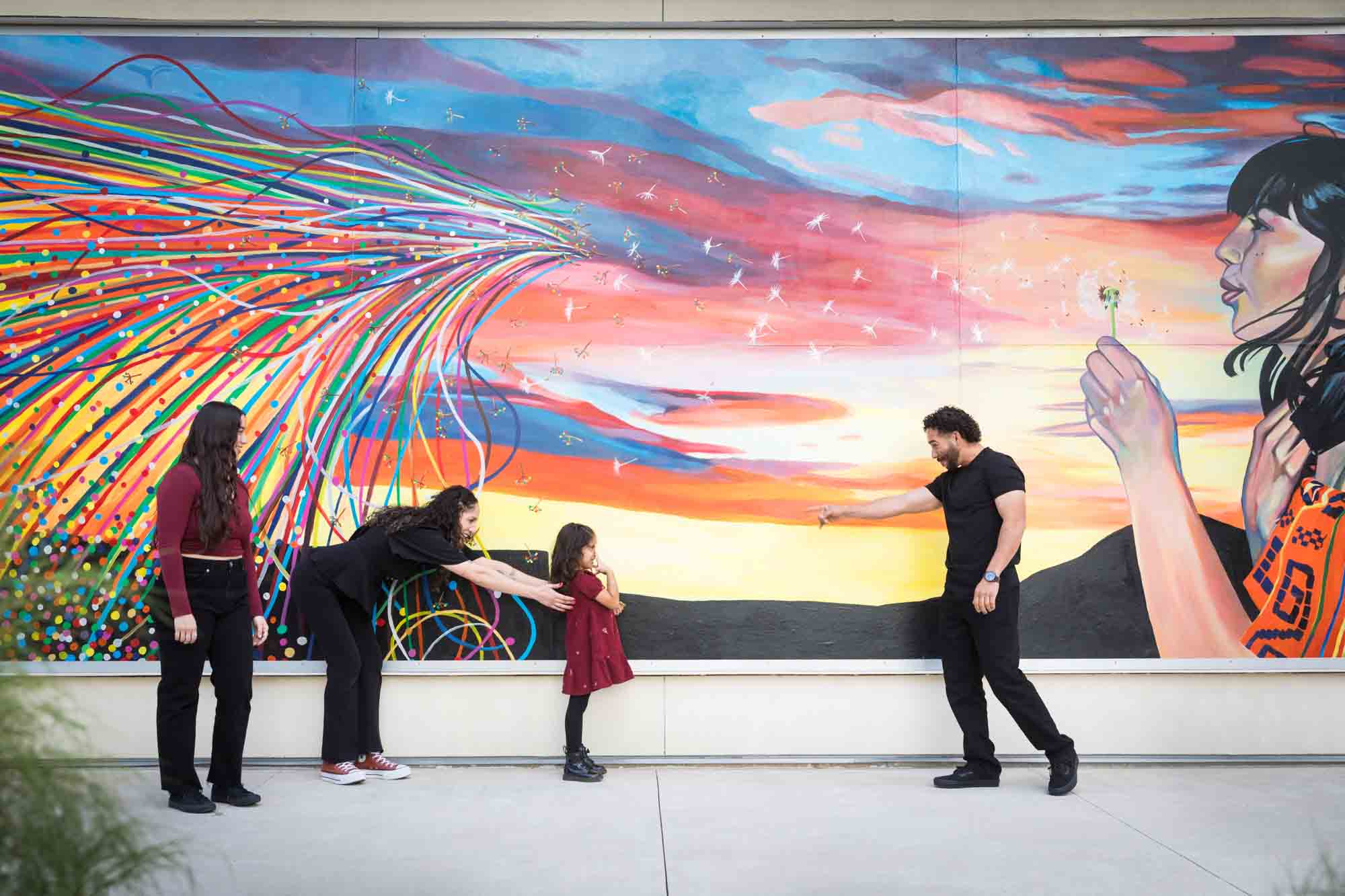 Family of two parents, teen girl and little girl playing in front of colorful mural by UTSA Data Sciences building