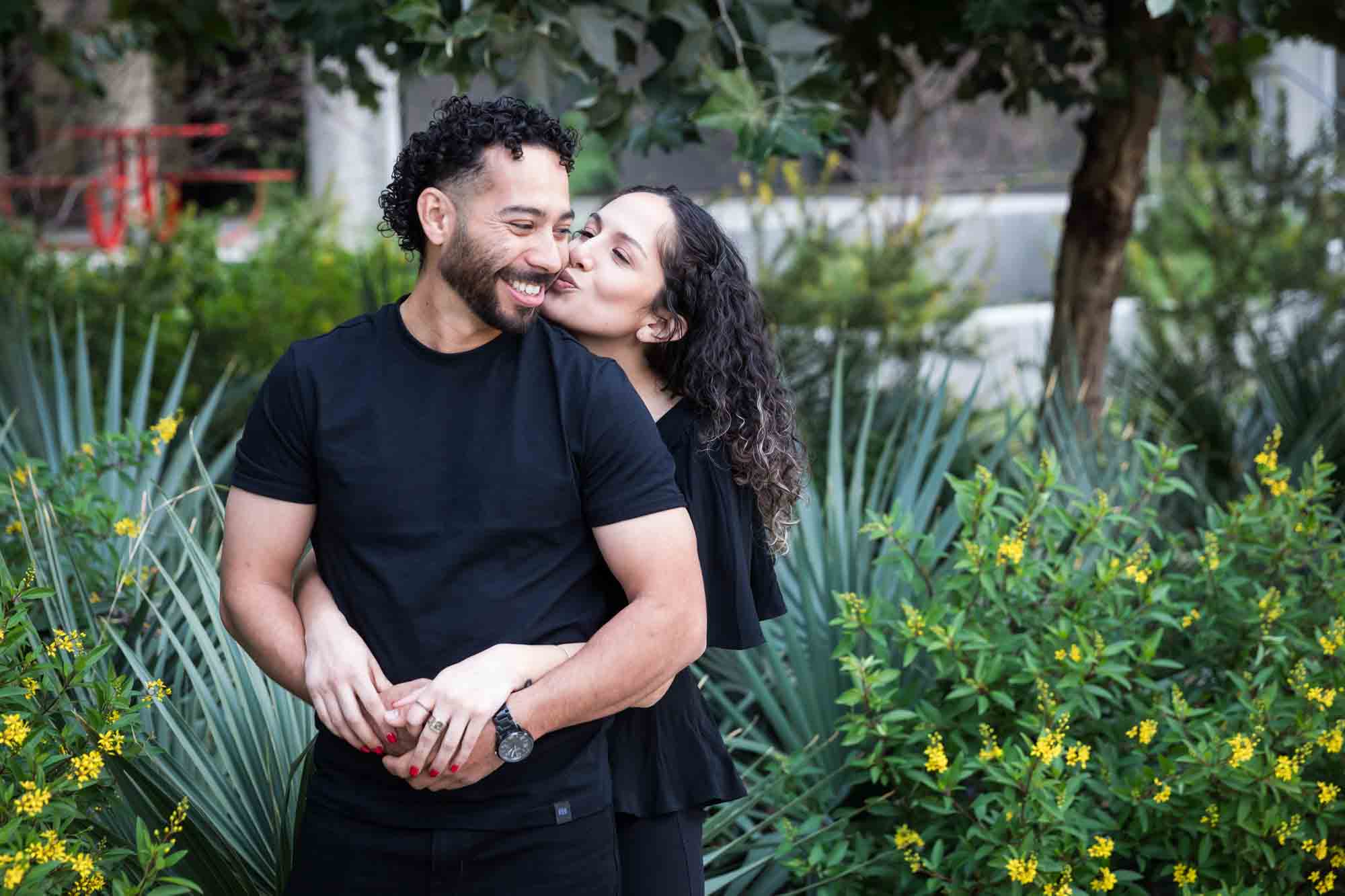 Couple wearing black t-shirts hugging in front of green bushes and palm fronds