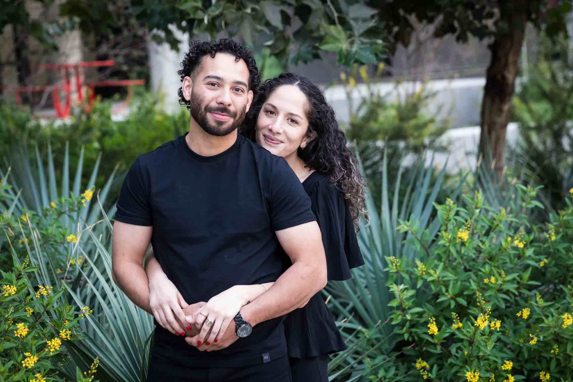 Couple wearing black t-shirts hugging in front of green bushes and palm fronds