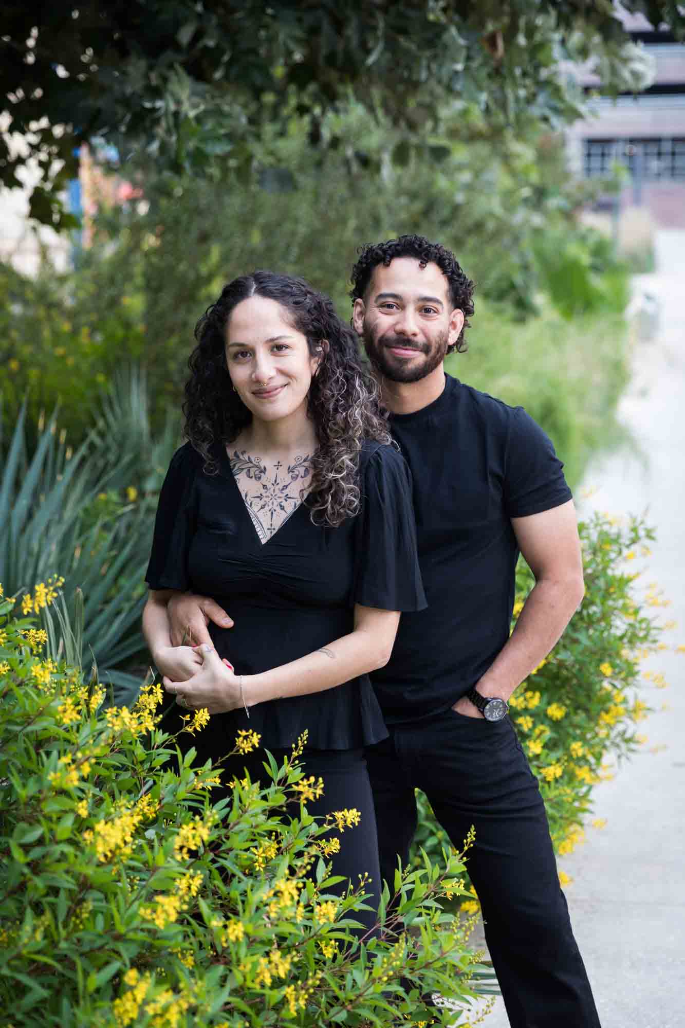 Couple wearing black t-shirts hugging in front of green bushes and palm fronds