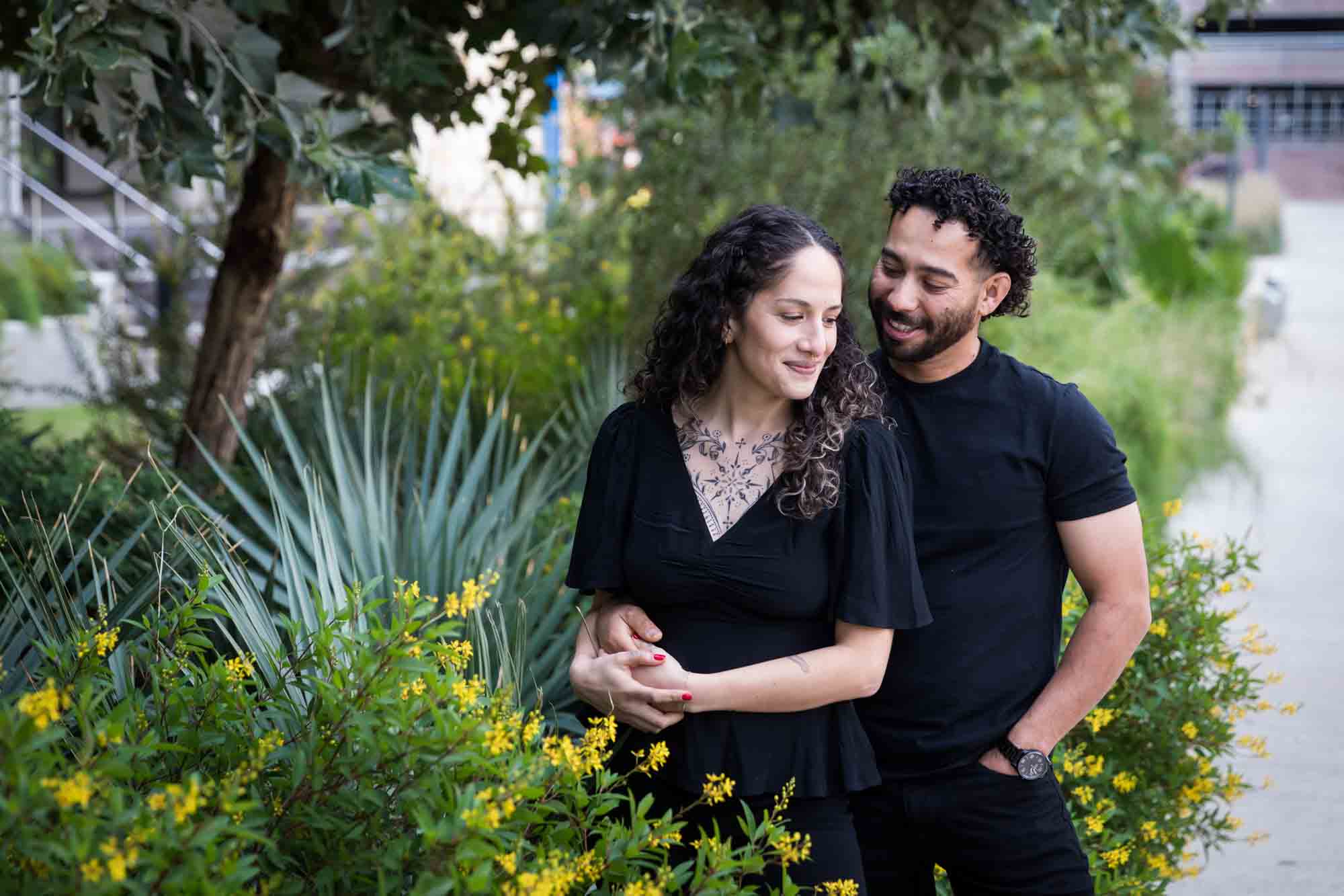 Couple wearing black t-shirts hugging in front of green bushes and palm fronds