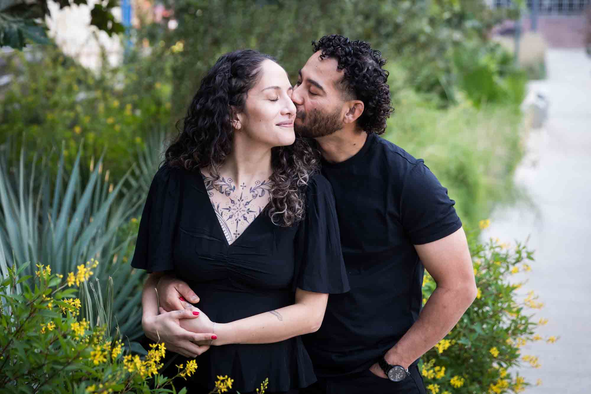 Couple wearing black t-shirts kissing in front of green bushes and palm fronds