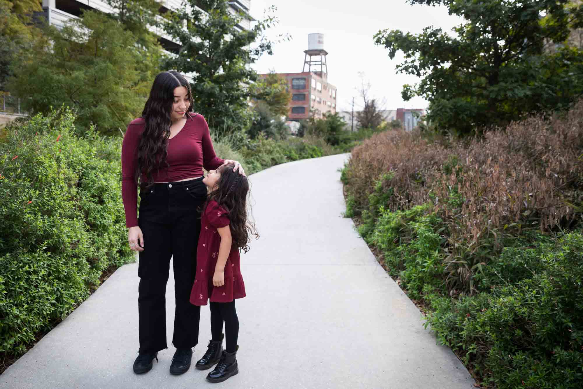 Older and younger sisters wearing maroon clothes with older girl touching younger girl's head