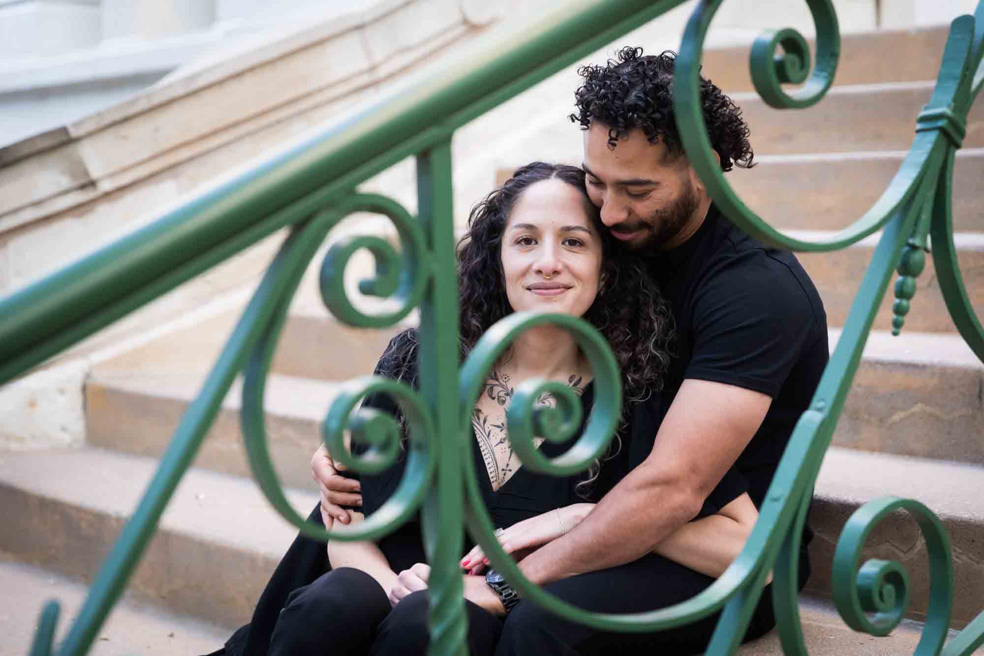 Couple wearing black t-shirts sitting closely on stairs behind green railing