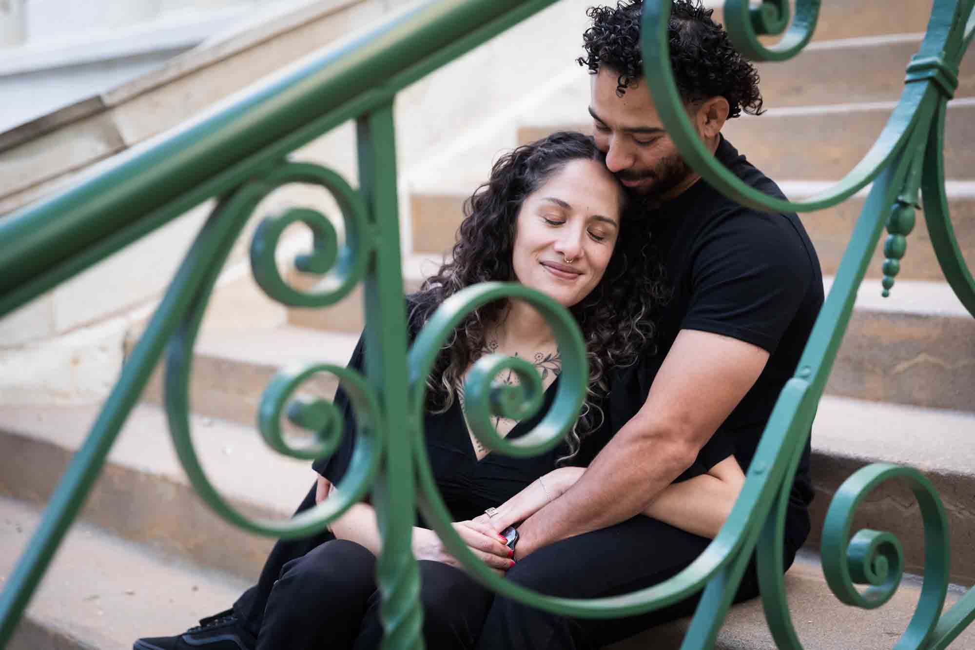 Couple wearing black t-shirts sitting closely on stairs behind green railing