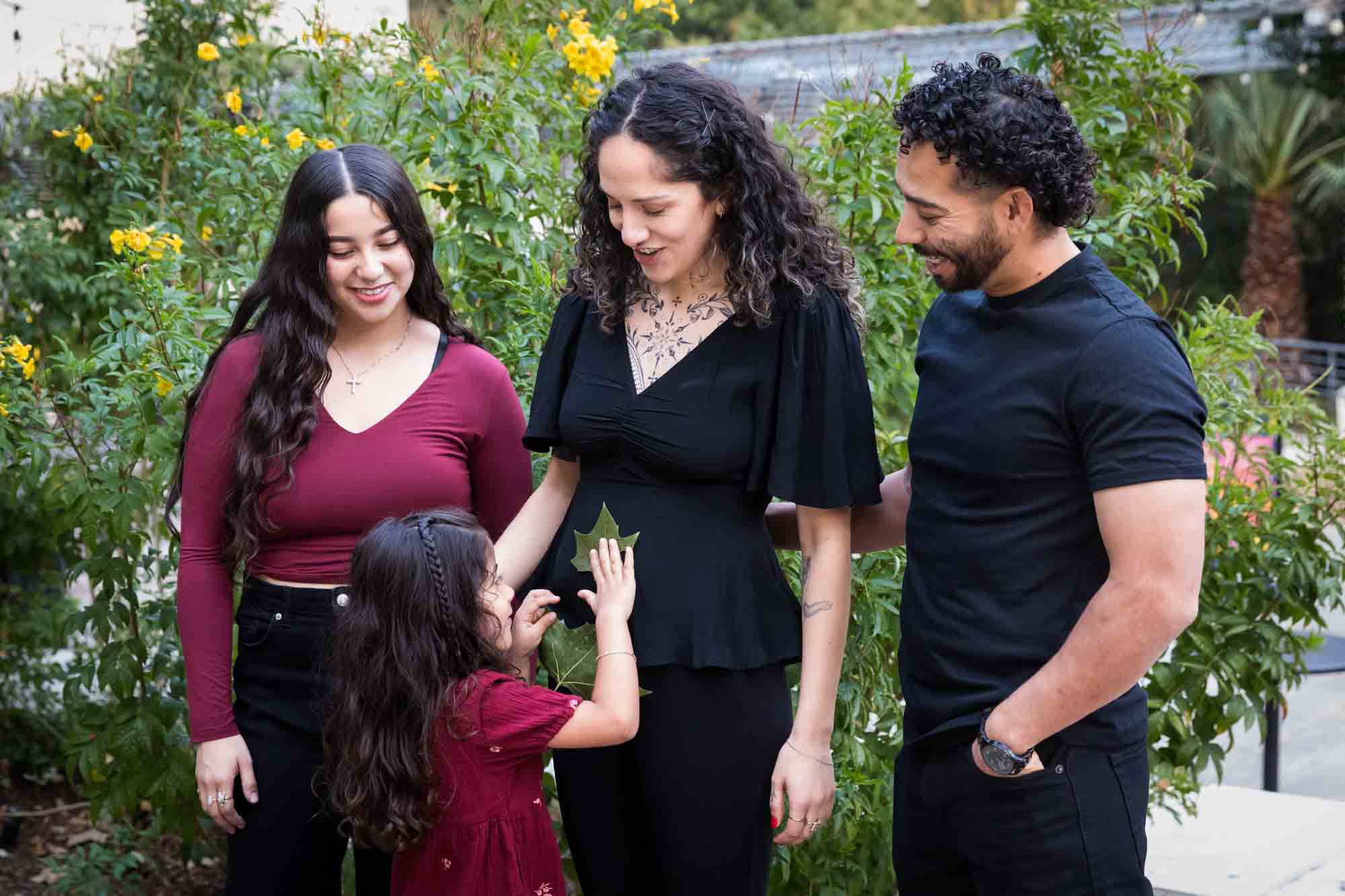 Parents standing with two girls as littles girl puts leaf on mom's belly