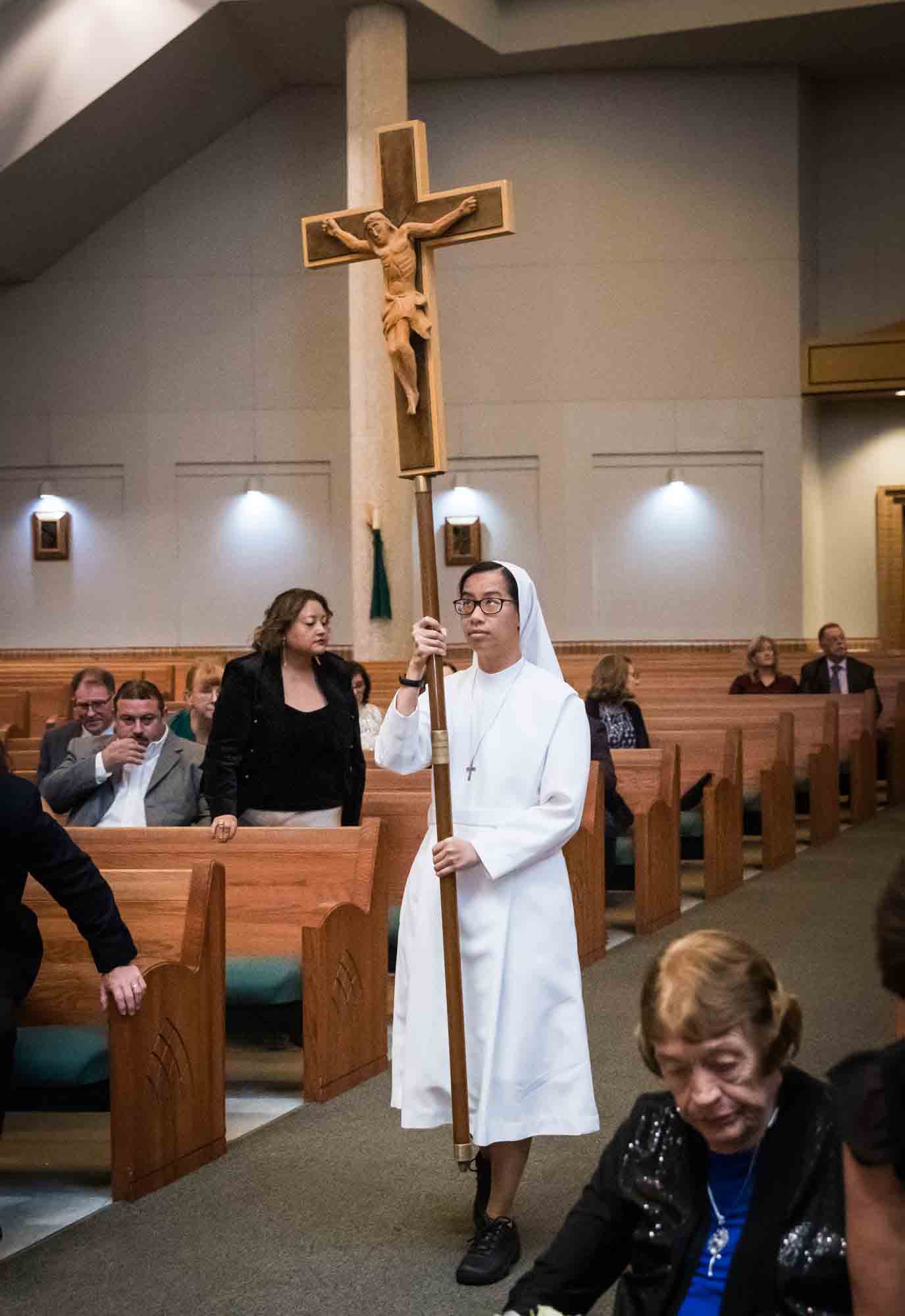 Nun carrying crucifix on a stick down the aisle at a St. Mark the Evangelist Catholic Church wedding