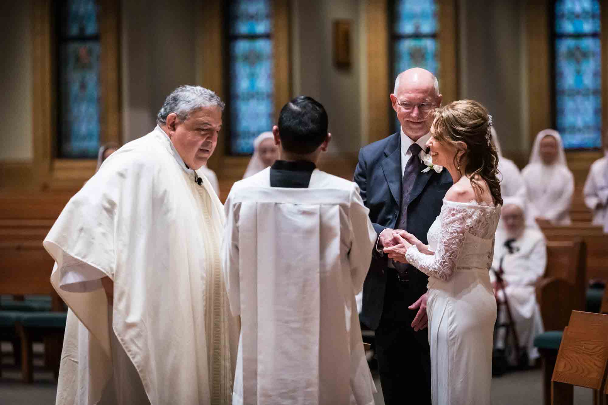 Priest and subordinate watching bride and groom say vows at a St. Mark the Evangelist Catholic Church wedding