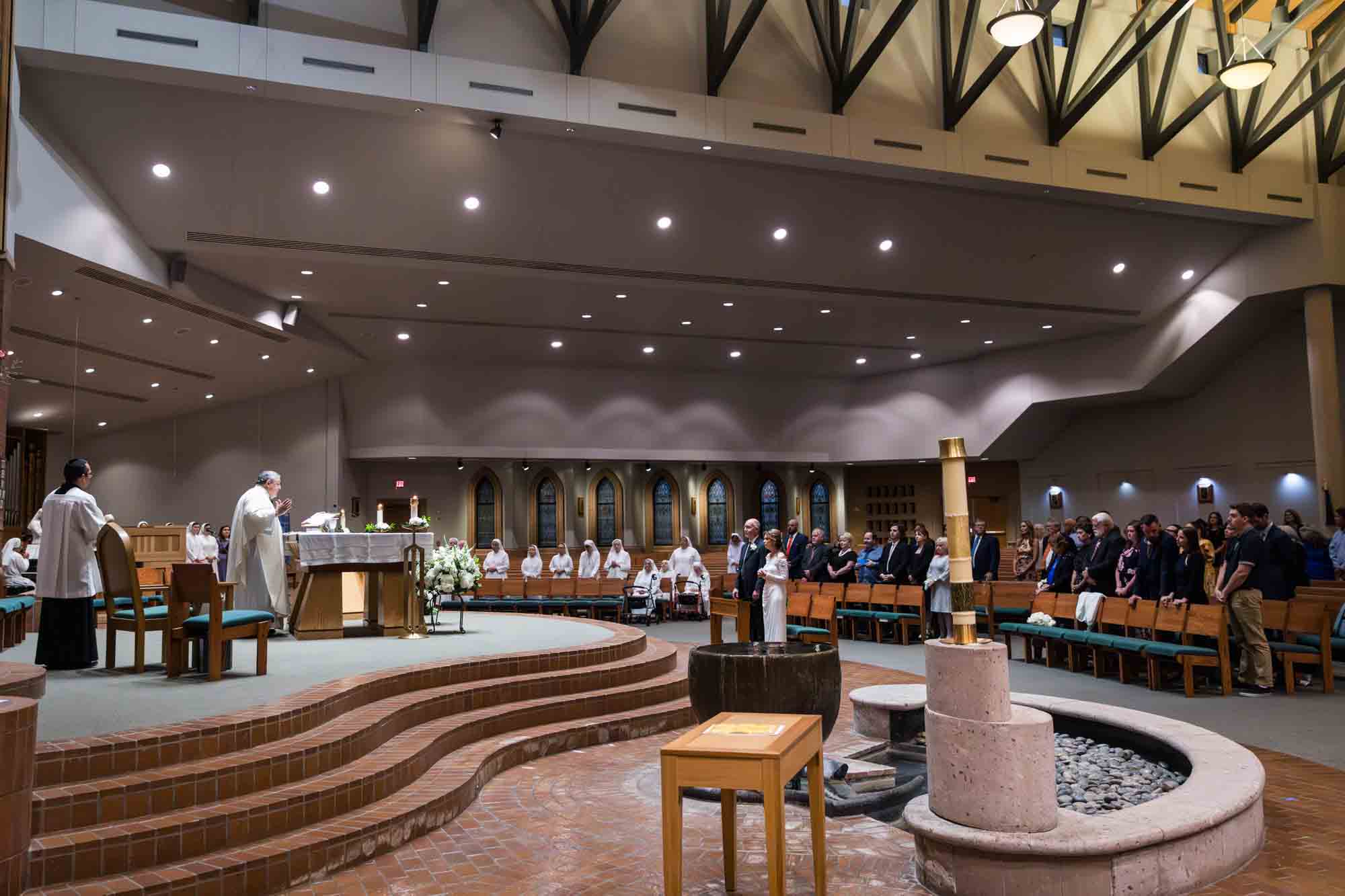 Wide shot of guests watching priest perform communion at a St. Mark the Evangelist Catholic Church wedding