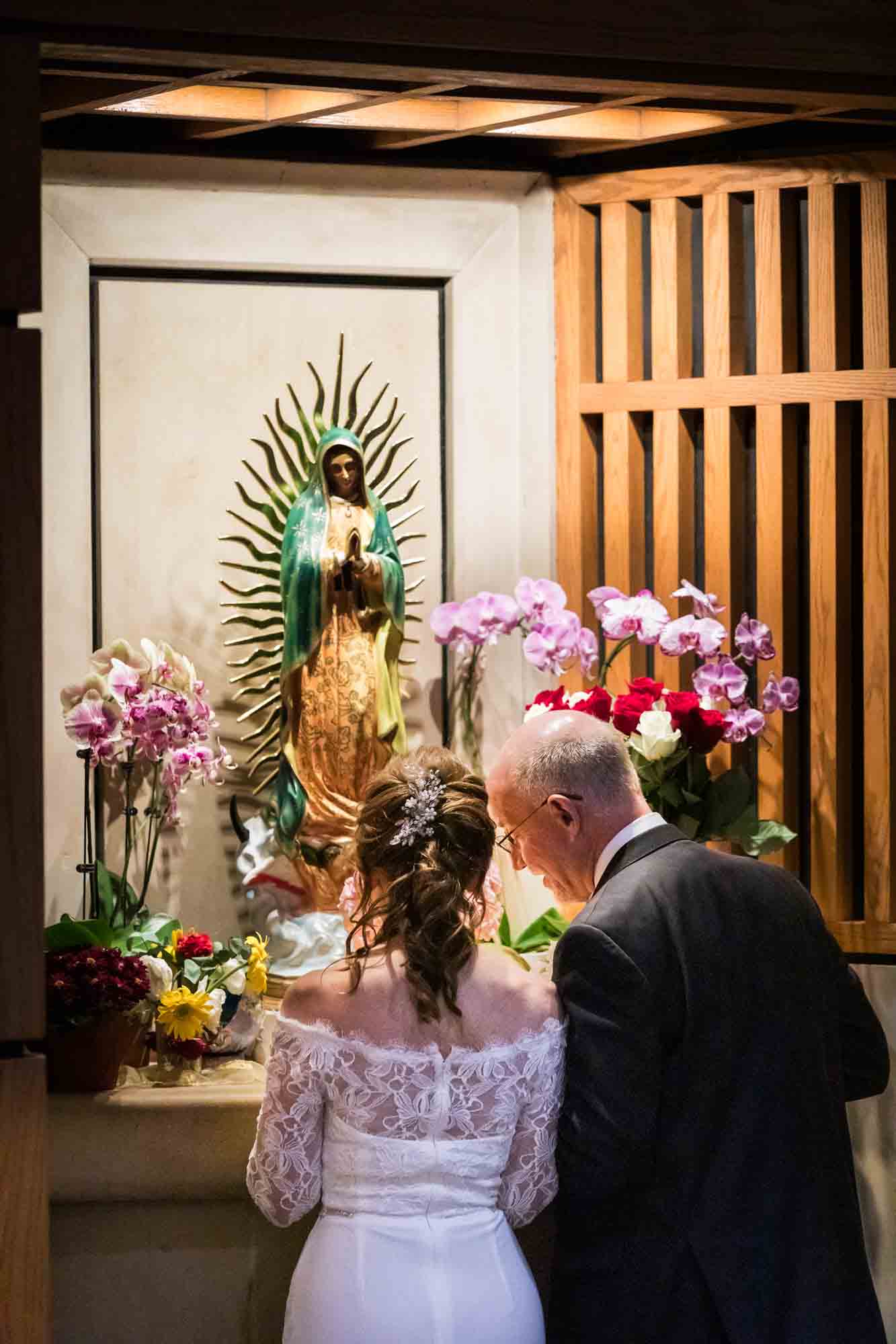 Bride and groom touching heads and speaking in front of statue of Mary at a St. Mark the Evangelist Catholic Church wedding