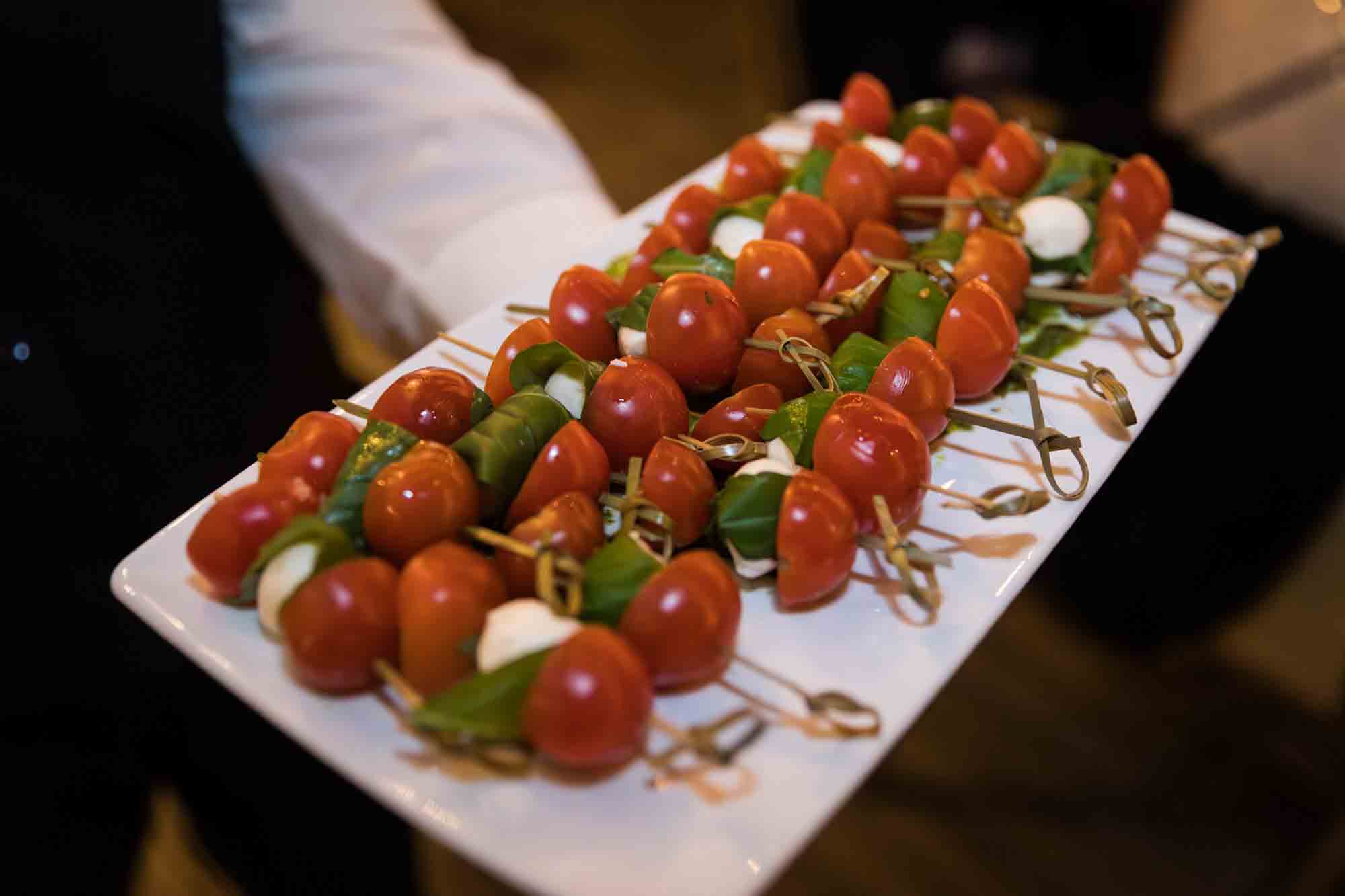 Close up of waiter holding white plate with rows of tomato appetizers