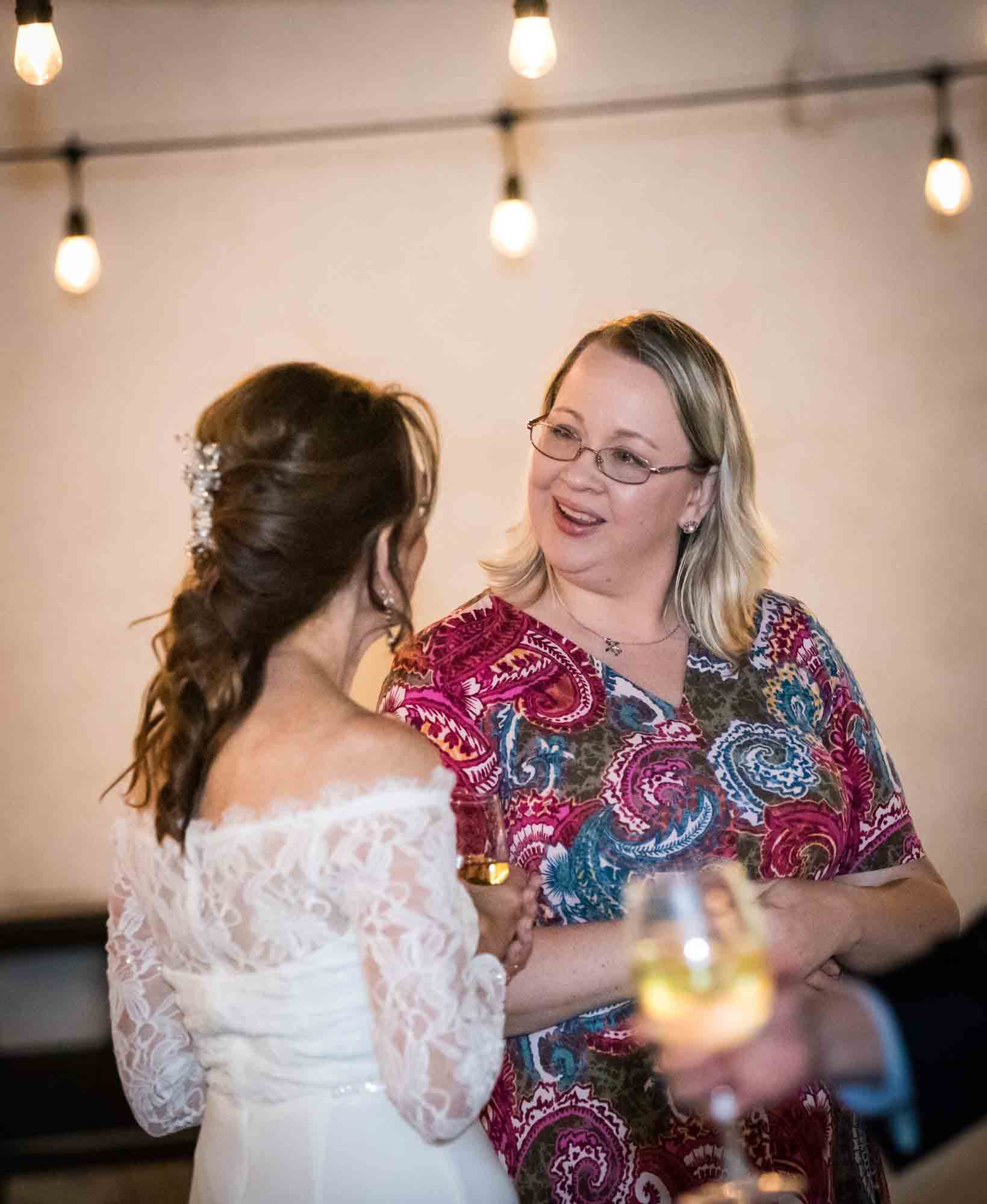 Bride speaking with blonde woman in pink floral dress during St. Anthony Hotel wedding reception