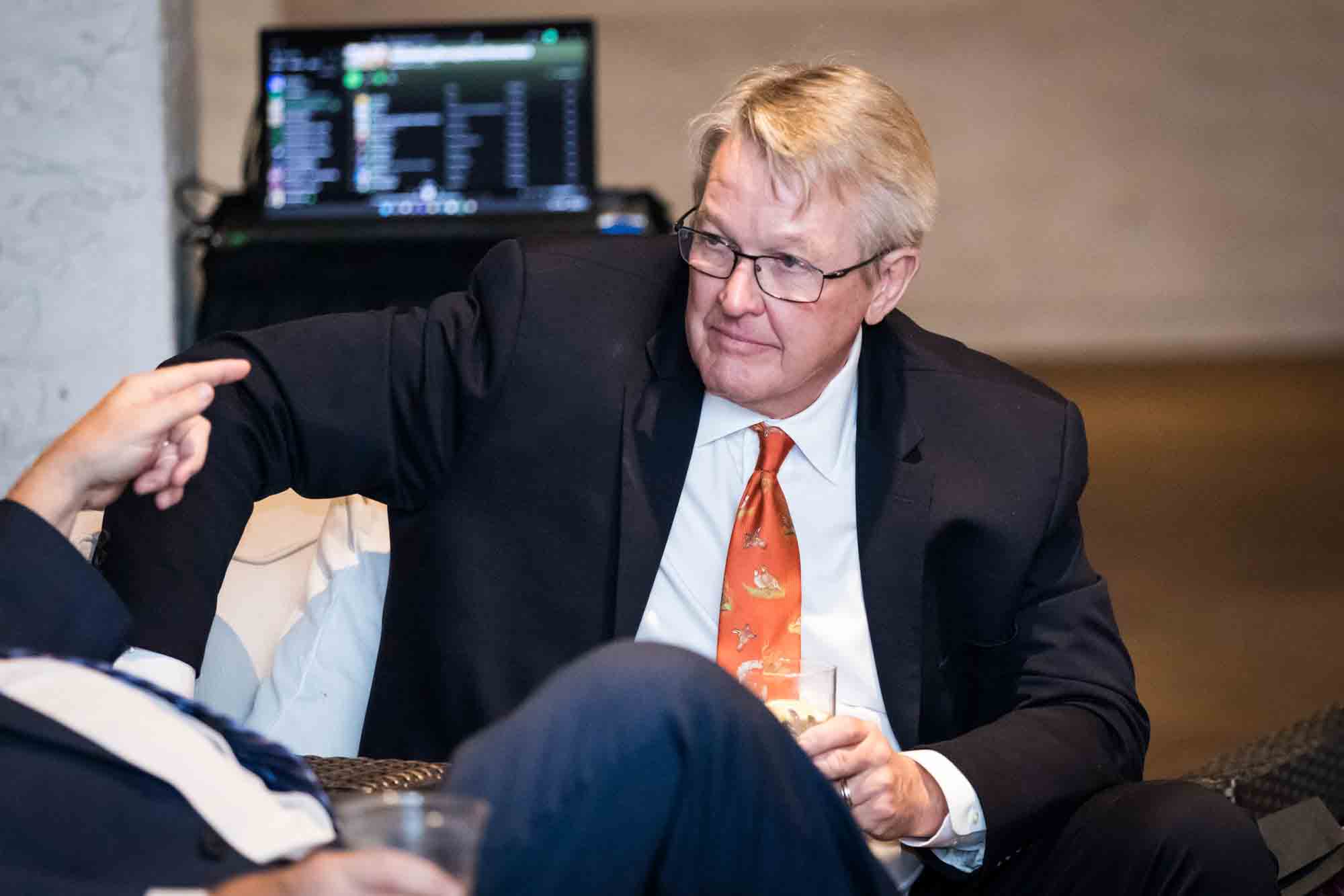 Man seated wearing black blazer and orange tie during St. Anthony Hotel wedding reception