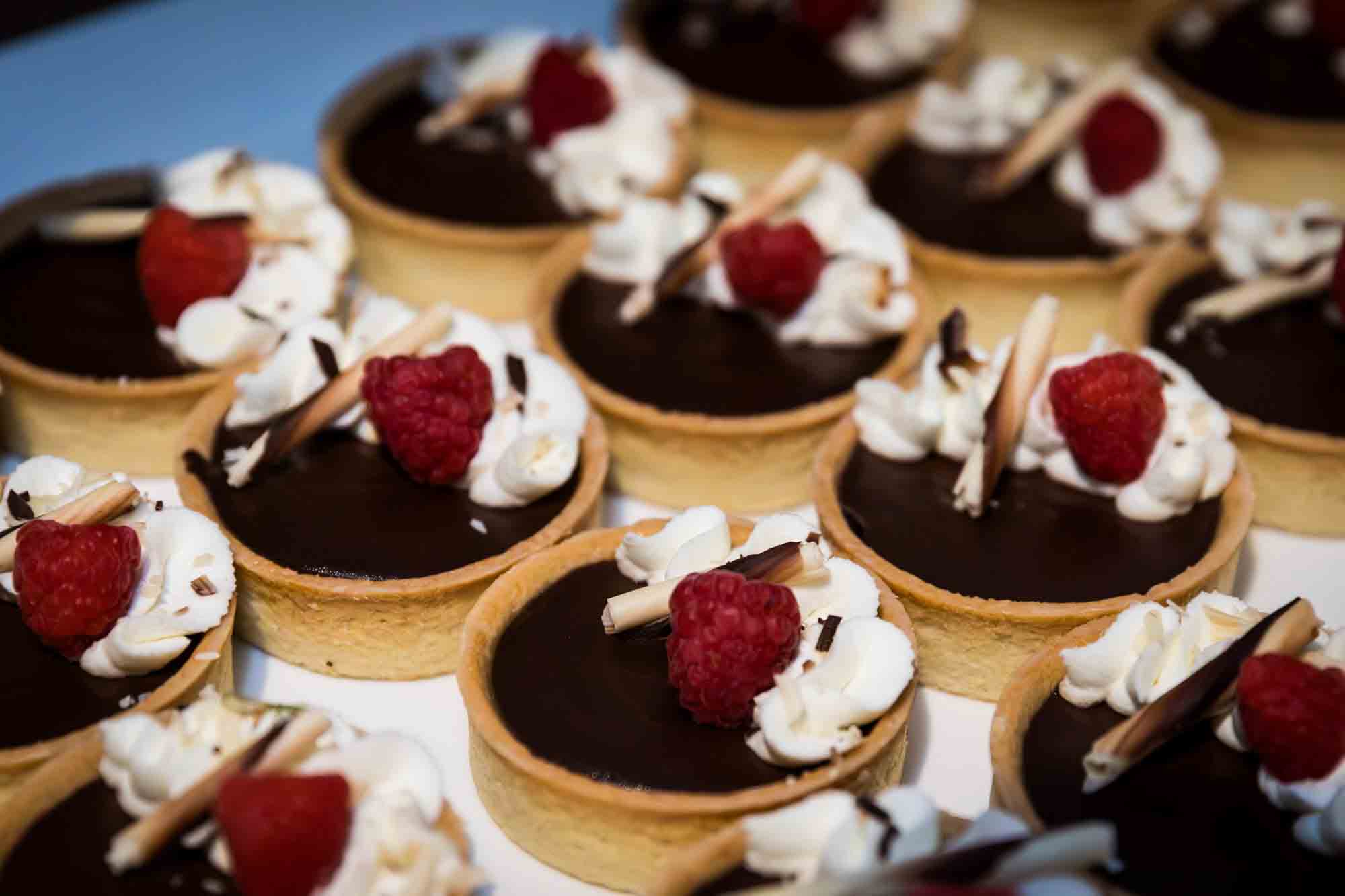 Close up of rows of chocolate desserts decorated with raspberries and whipped cream