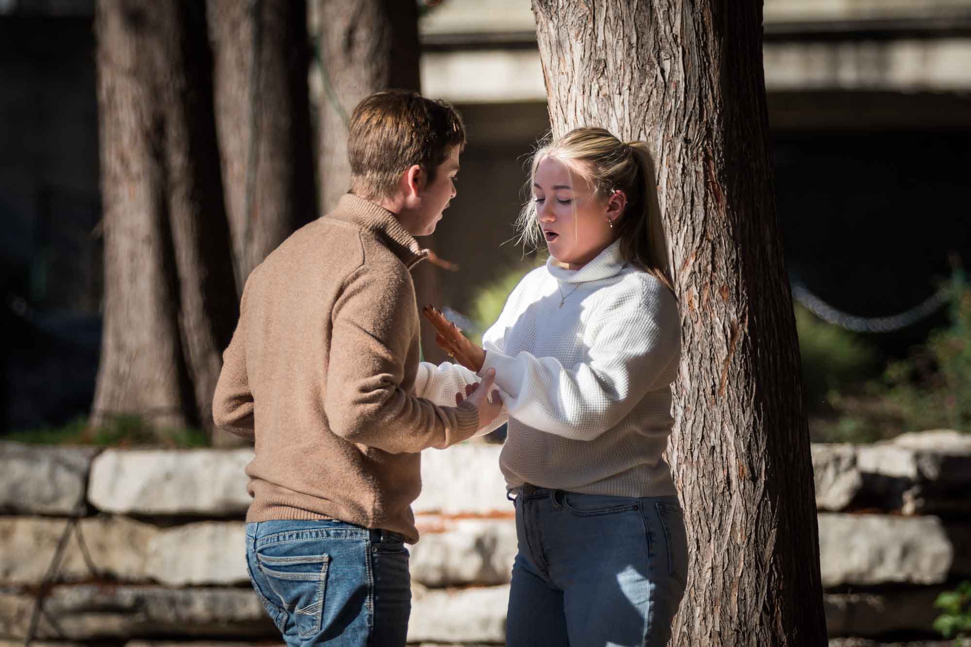 Man holding woman's hand as she looks at hand wearing engagement ring for an article on the importance of timing for a surprise proposal