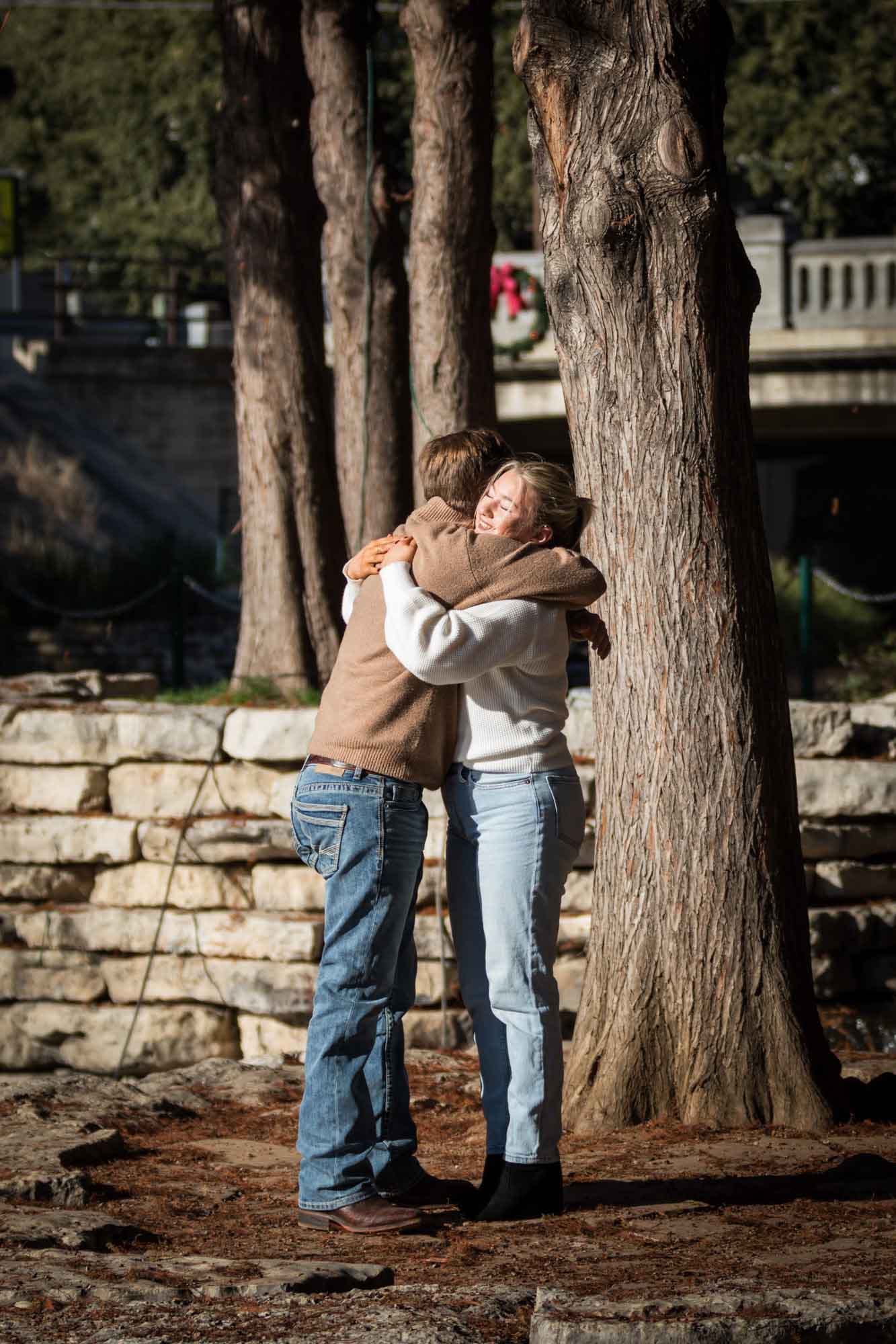 Couple hugging on Pearl Springs island in front of trees for an article on the importance of timing for a surprise proposal