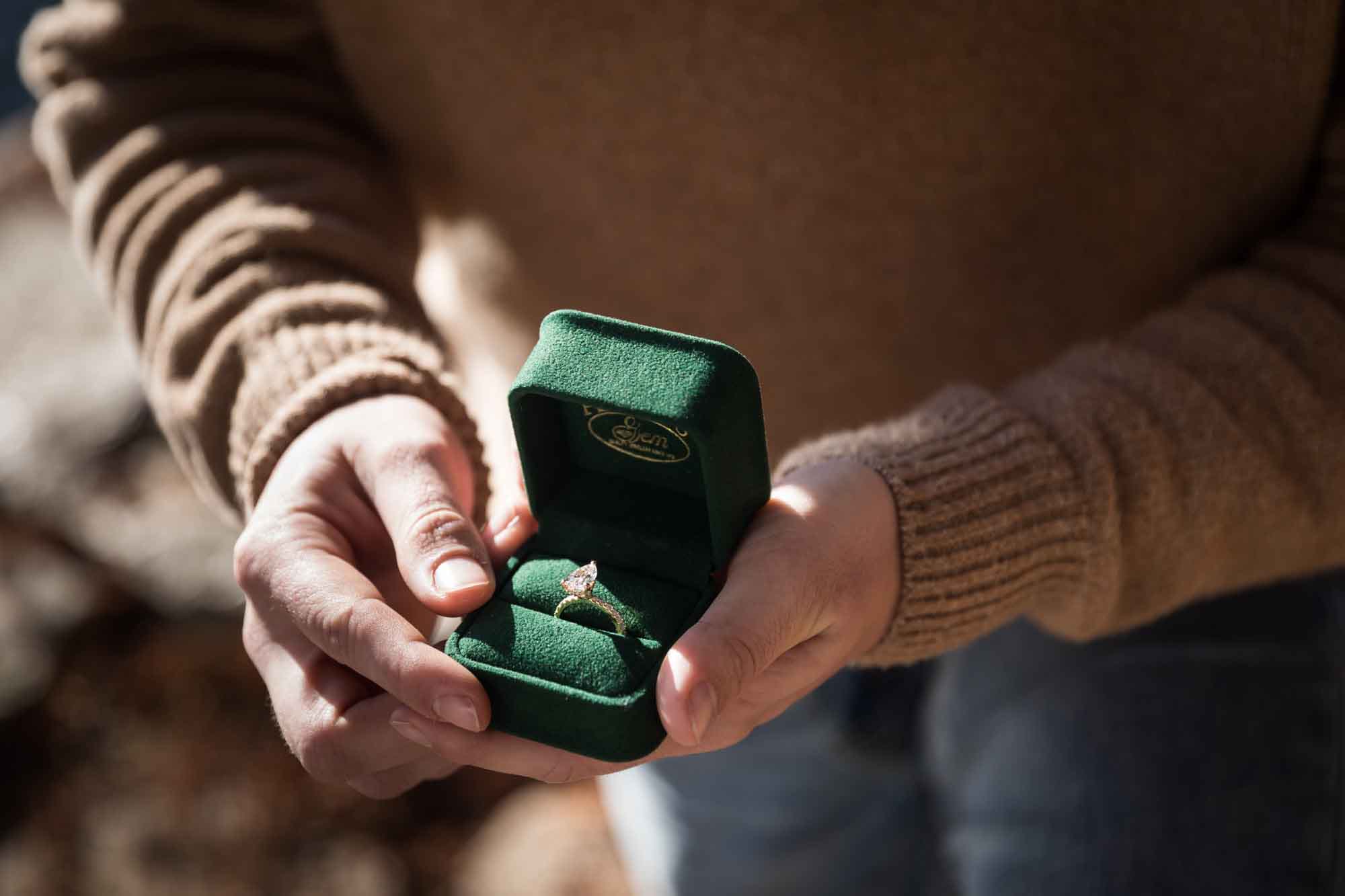 Close up of man's hand holding green ring box with engagement ring for an article on the importance of timing for a surprise proposal