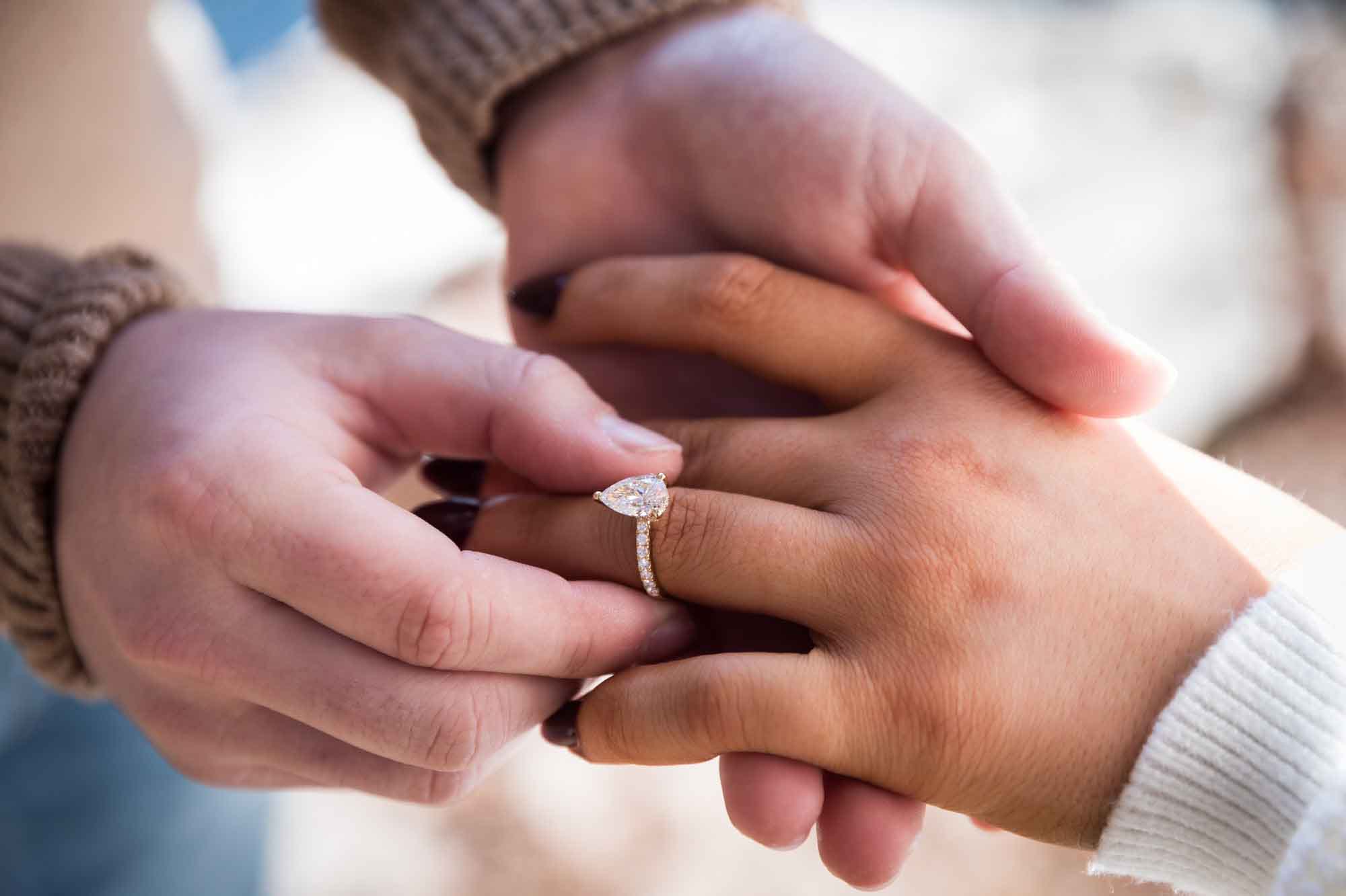 Close up of man putting engagement ring on woman's hand for an article on the importance of timing for a surprise proposal