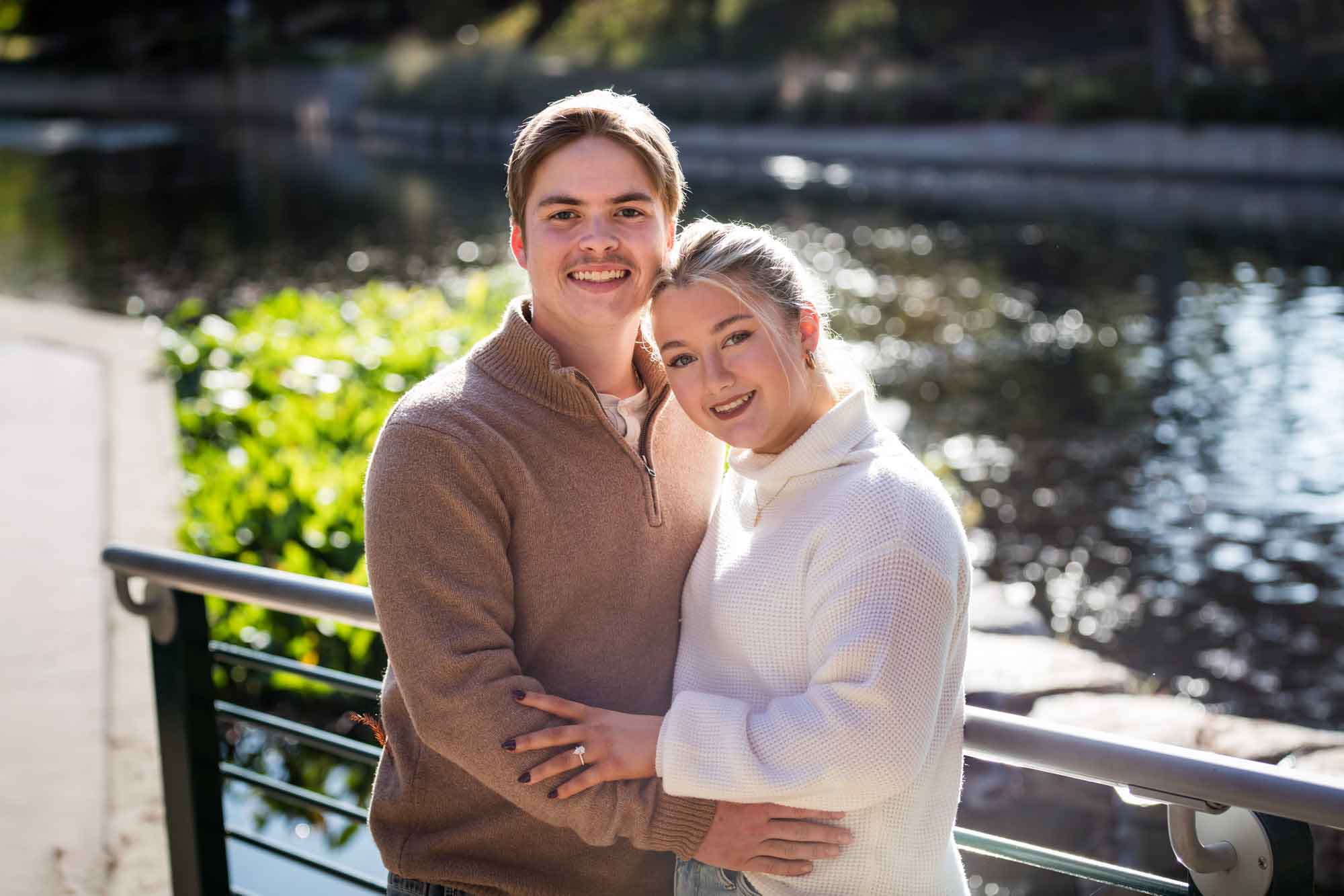 Couple wearing sweaters and hugging in front of the Riverwalk at the Pearl during an engagement photo shoot