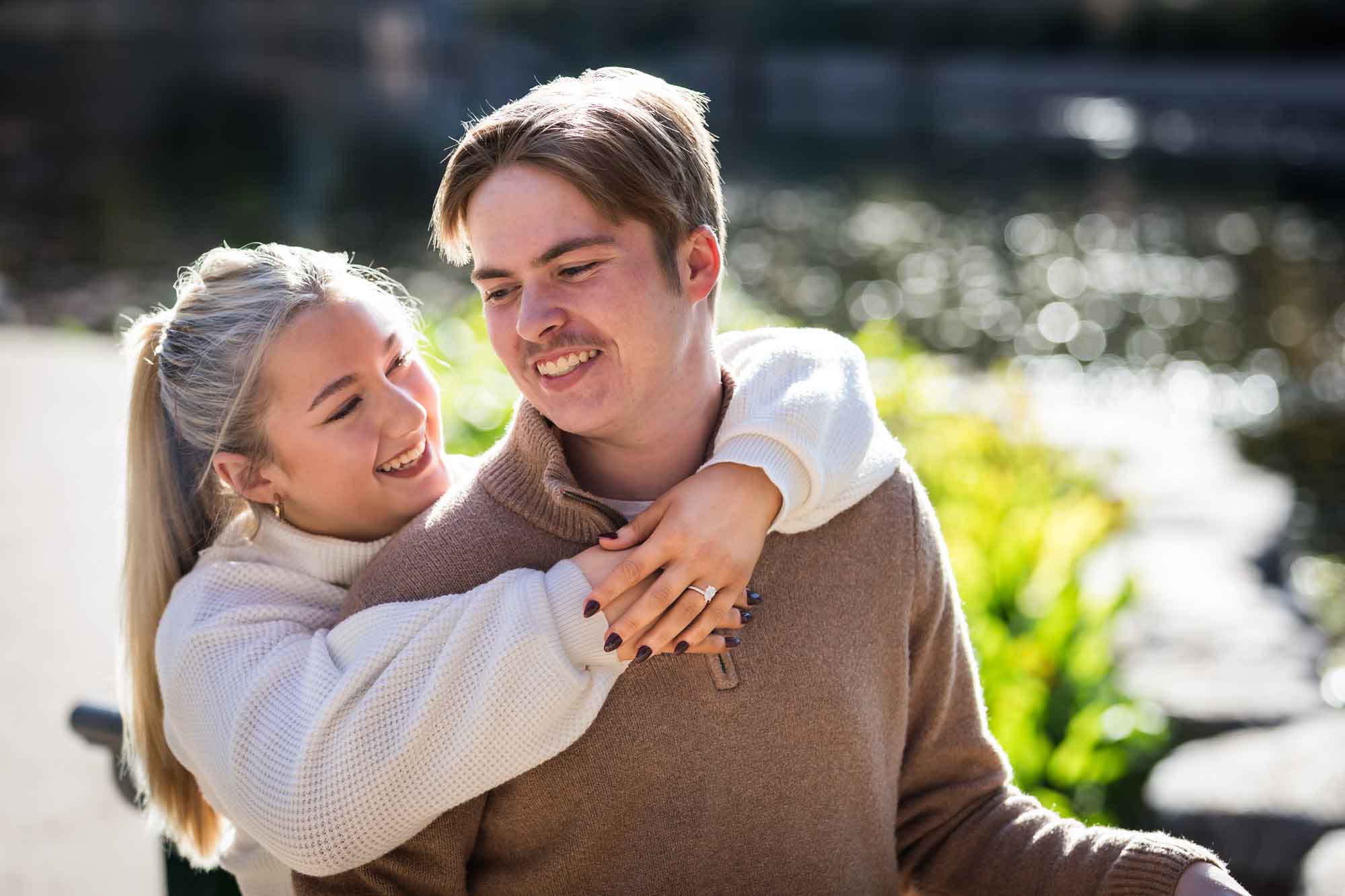 Couple wearing sweaters and hugging in front of the Riverwalk at the Pearl during an engagement photo shoot