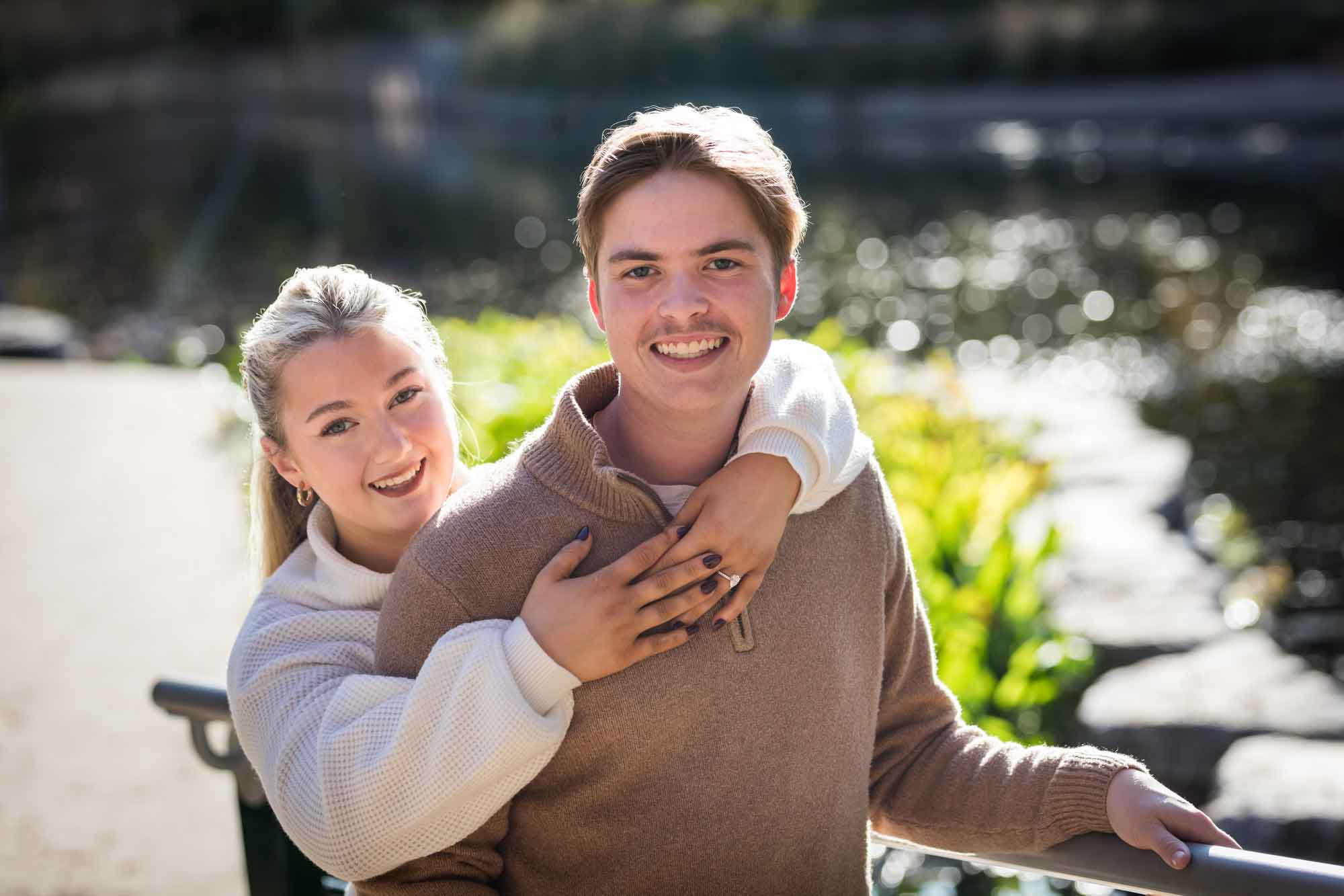 Couple wearing sweaters and hugging in front of the Riverwalk at the Pearl during an engagement photo shoot