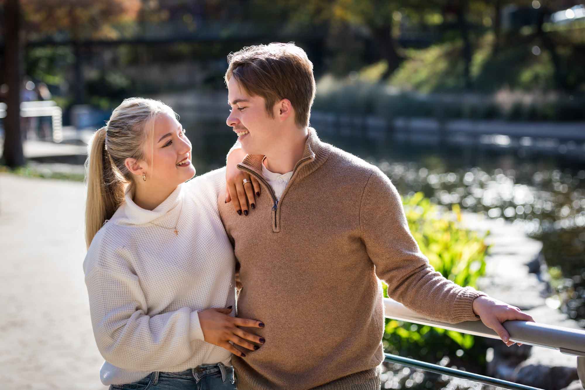 Couple wearing sweaters and hugging in front of the Riverwalk at the Pearl during an engagement photo shoot