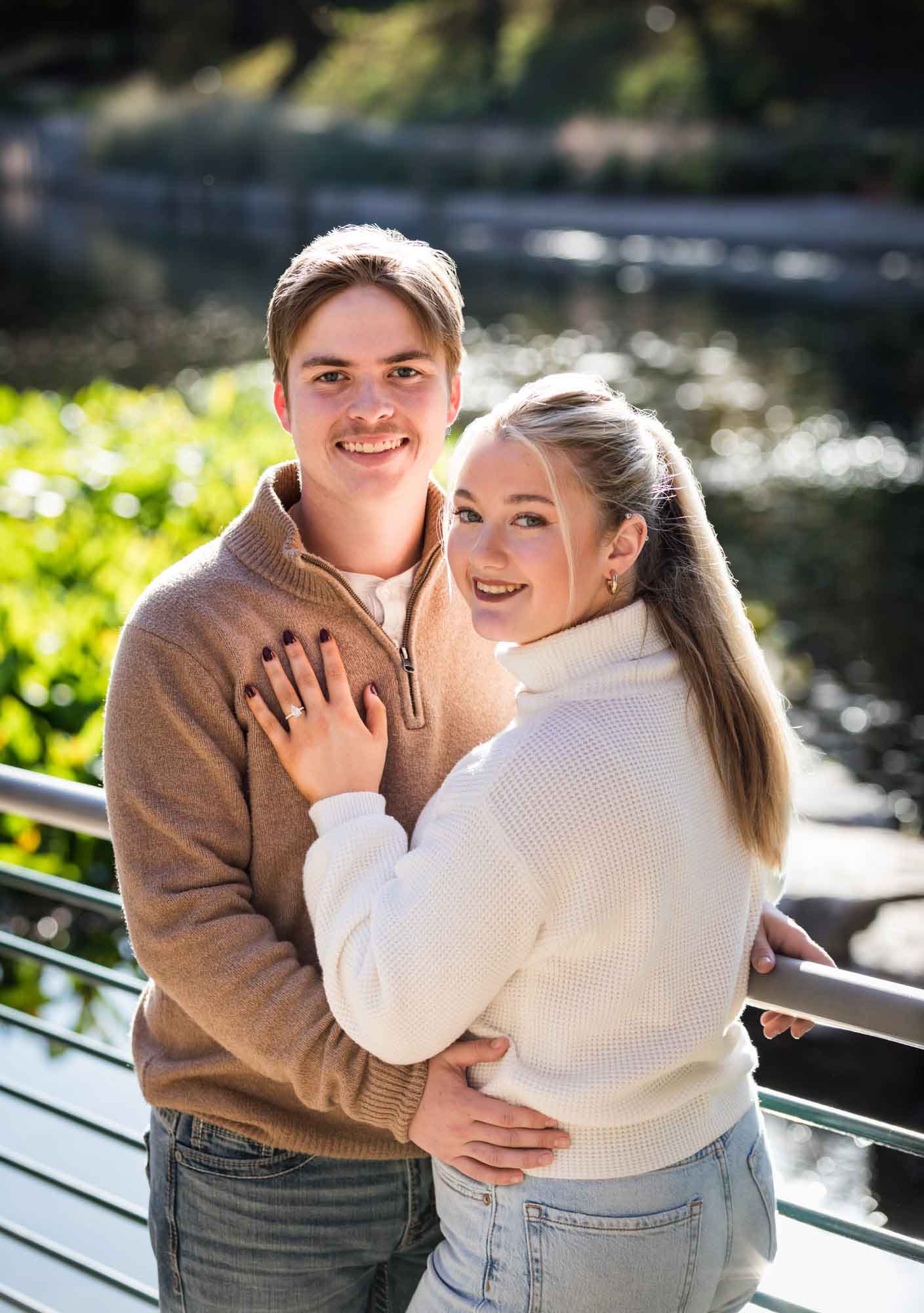 Couple wearing sweaters and hugging in front of the Riverwalk at the Pearl during an engagement photo shoot