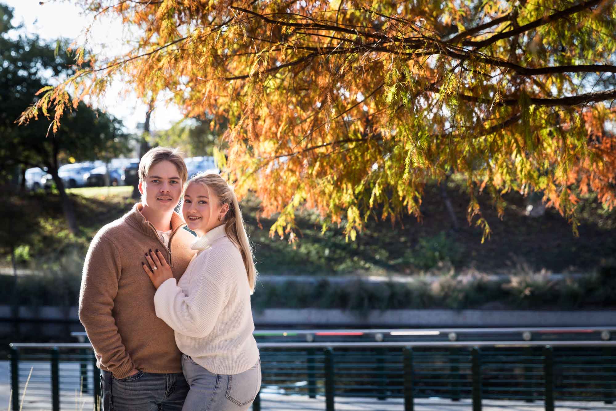 Couple wearing sweaters and hugging in front of colorful leaves at the Pearl during an engagement photo shoot