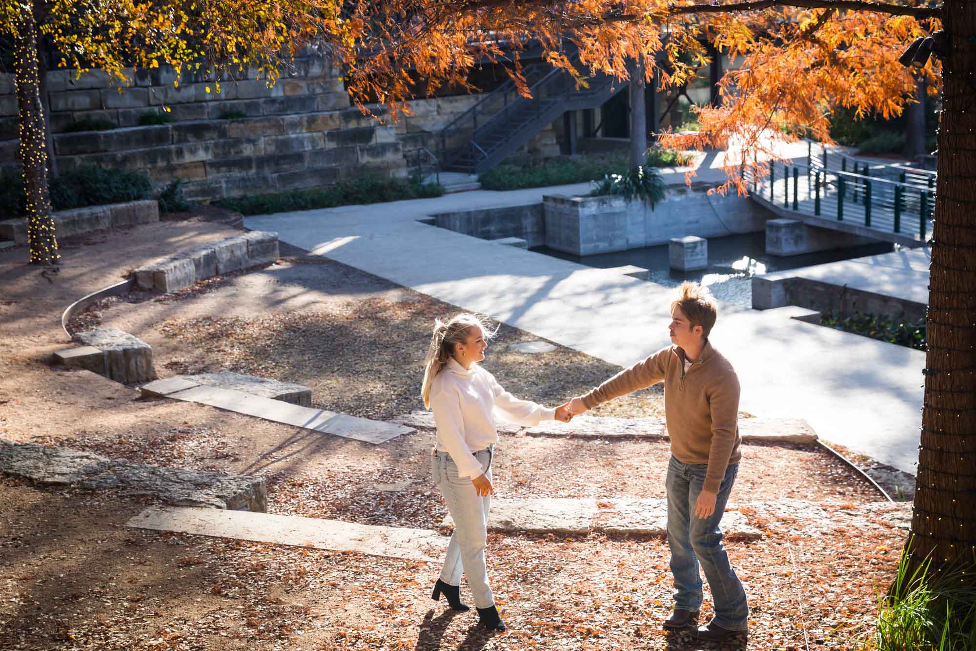 Couple wearing sweaters and dancing in front of colorful leaves at the Pearl during an engagement photo shoot