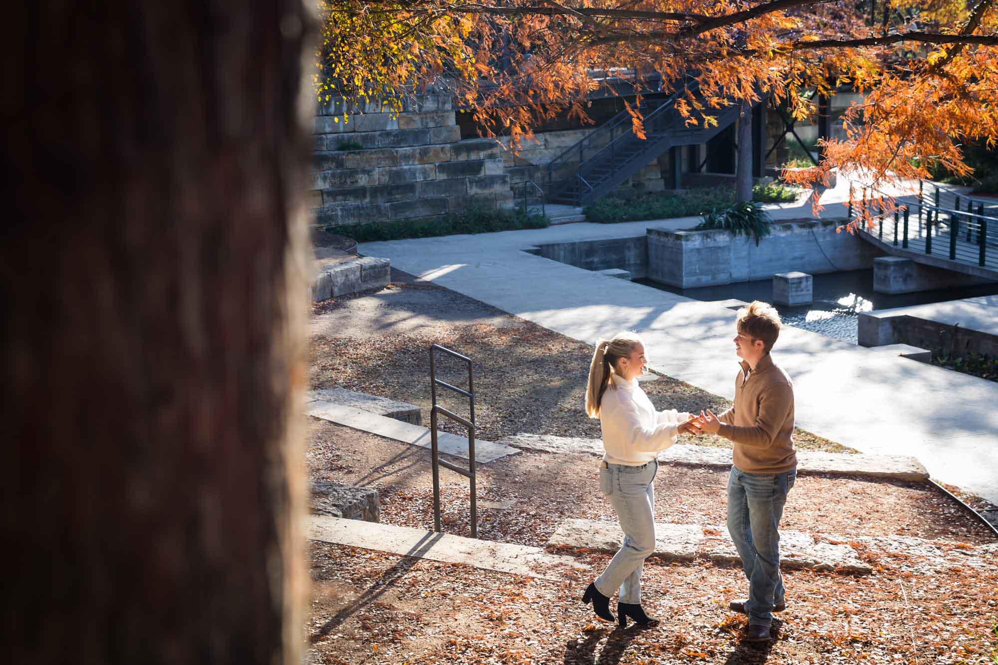 Couple wearing sweaters and dancing in front of colorful leaves at the Pearl during an engagement photo shoot