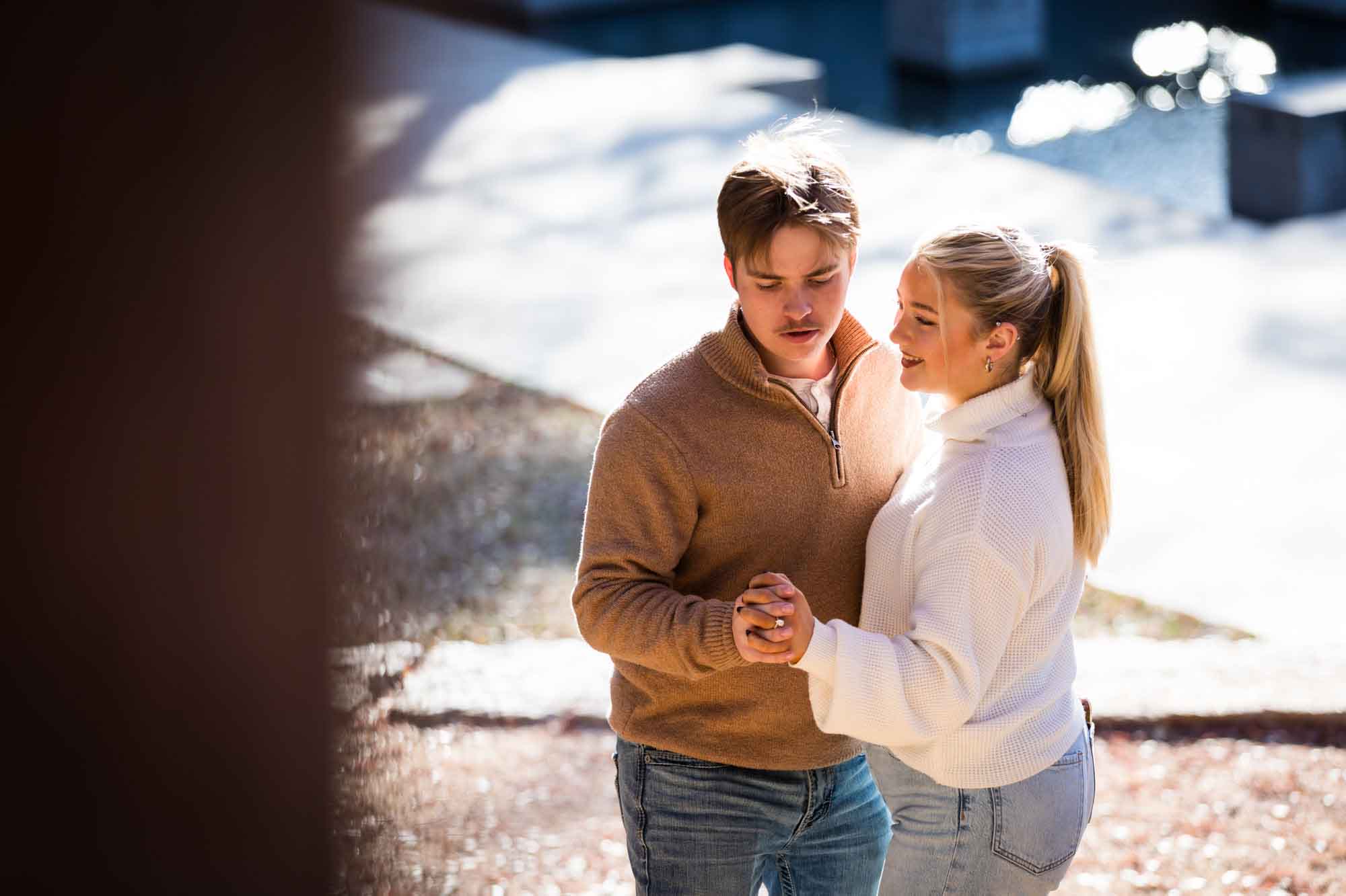 Couple wearing sweaters and dancing in front of the Riverwalk at the Pearl during an engagement photo shoot