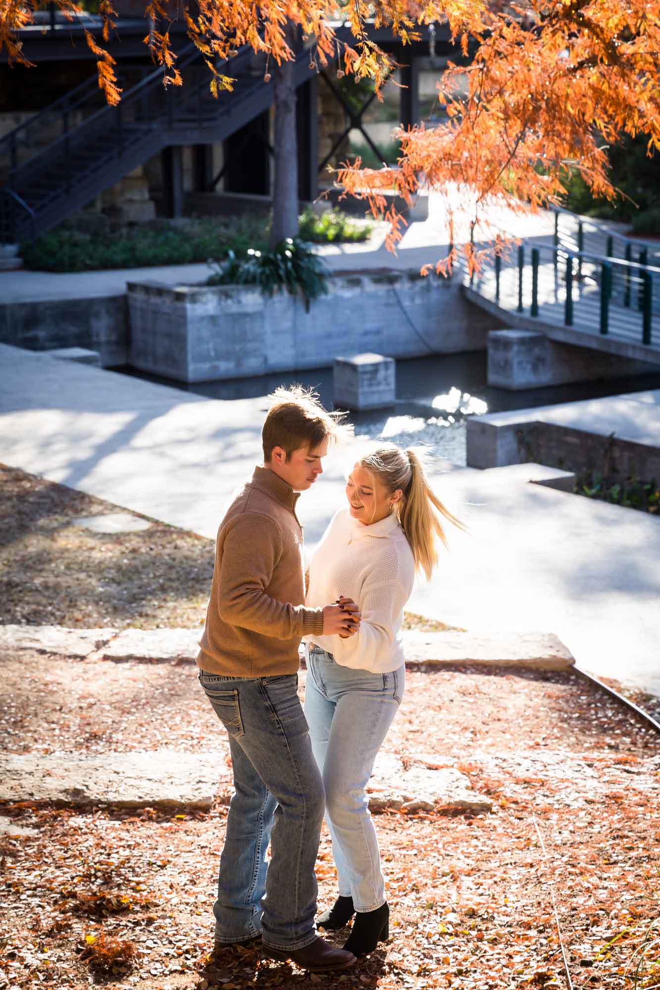 Couple wearing sweaters and dancing in front of the Riverwalk at the Pearl during an engagement photo shoot