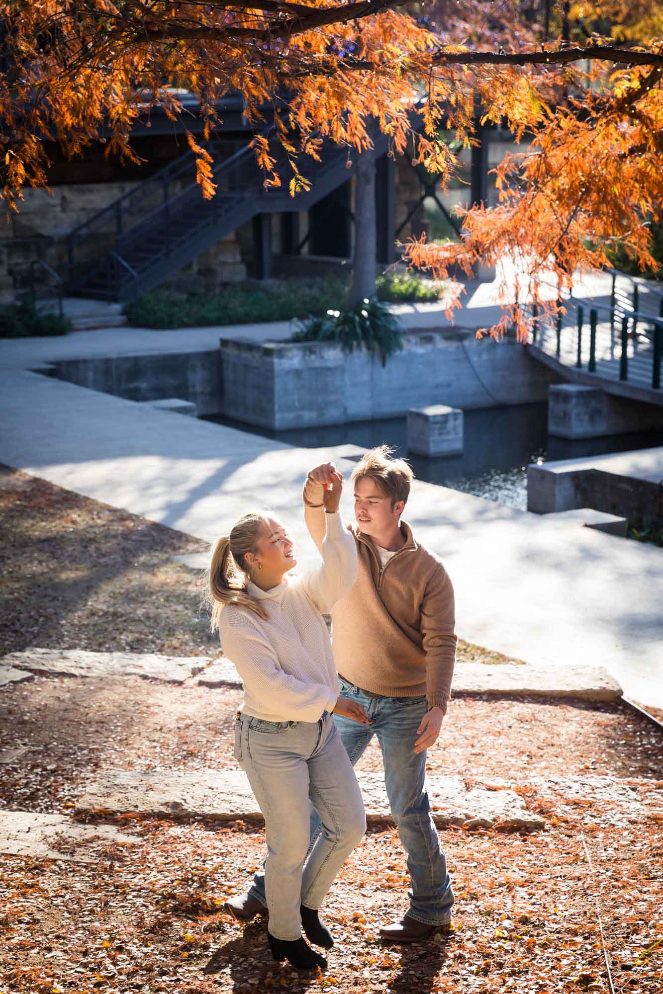 Couple wearing sweaters and dancing in front of the Riverwalk at the Pearl during an engagement photo shoot