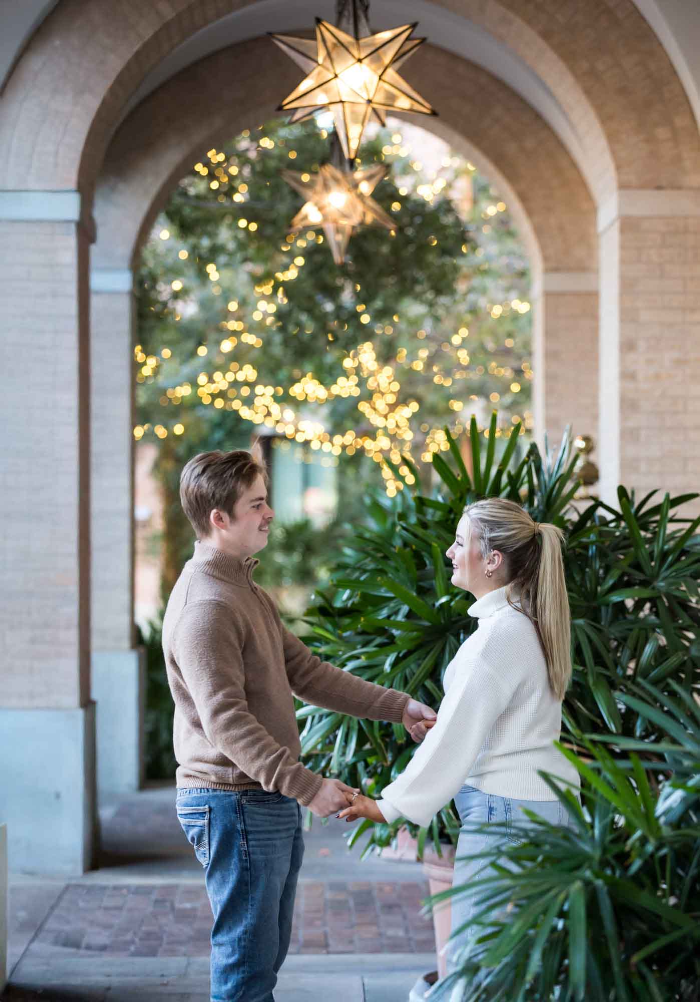 Couple wearing sweaters and dancing under brick arch with star lanterns at the Pearl during an engagement photo shoot