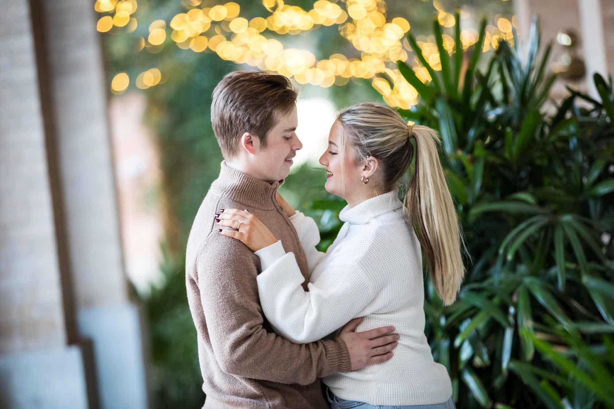 Couple wearing sweaters and hugging in front of string lights at the Pearl during an engagement photo shoot