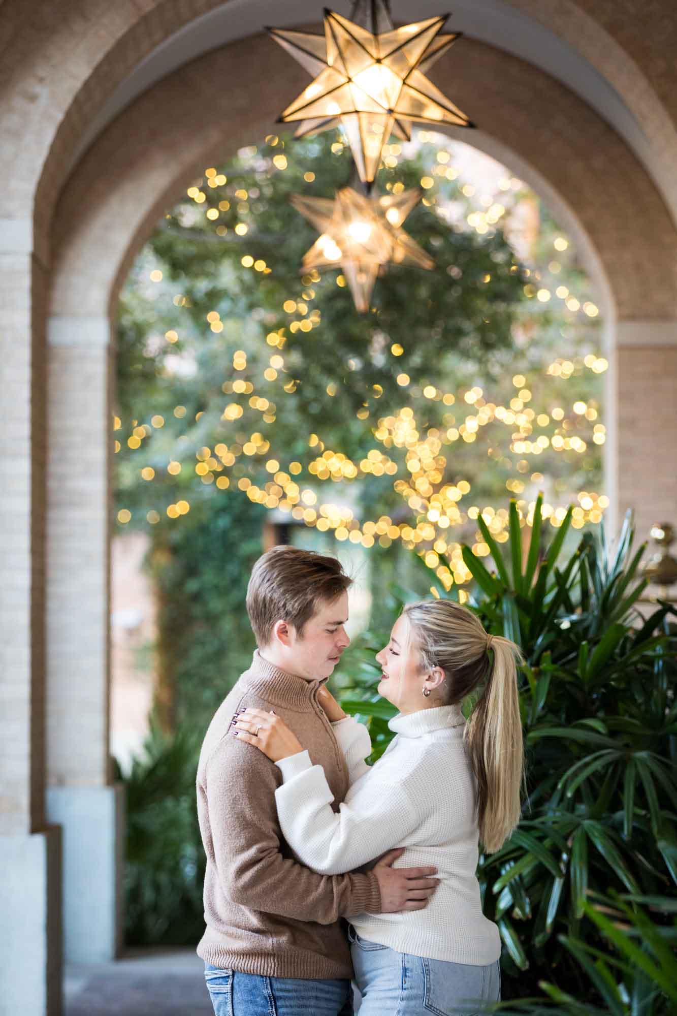 Couple wearing sweaters and dancing under brick arch with star lanterns at the Pearl during an engagement photo shoot