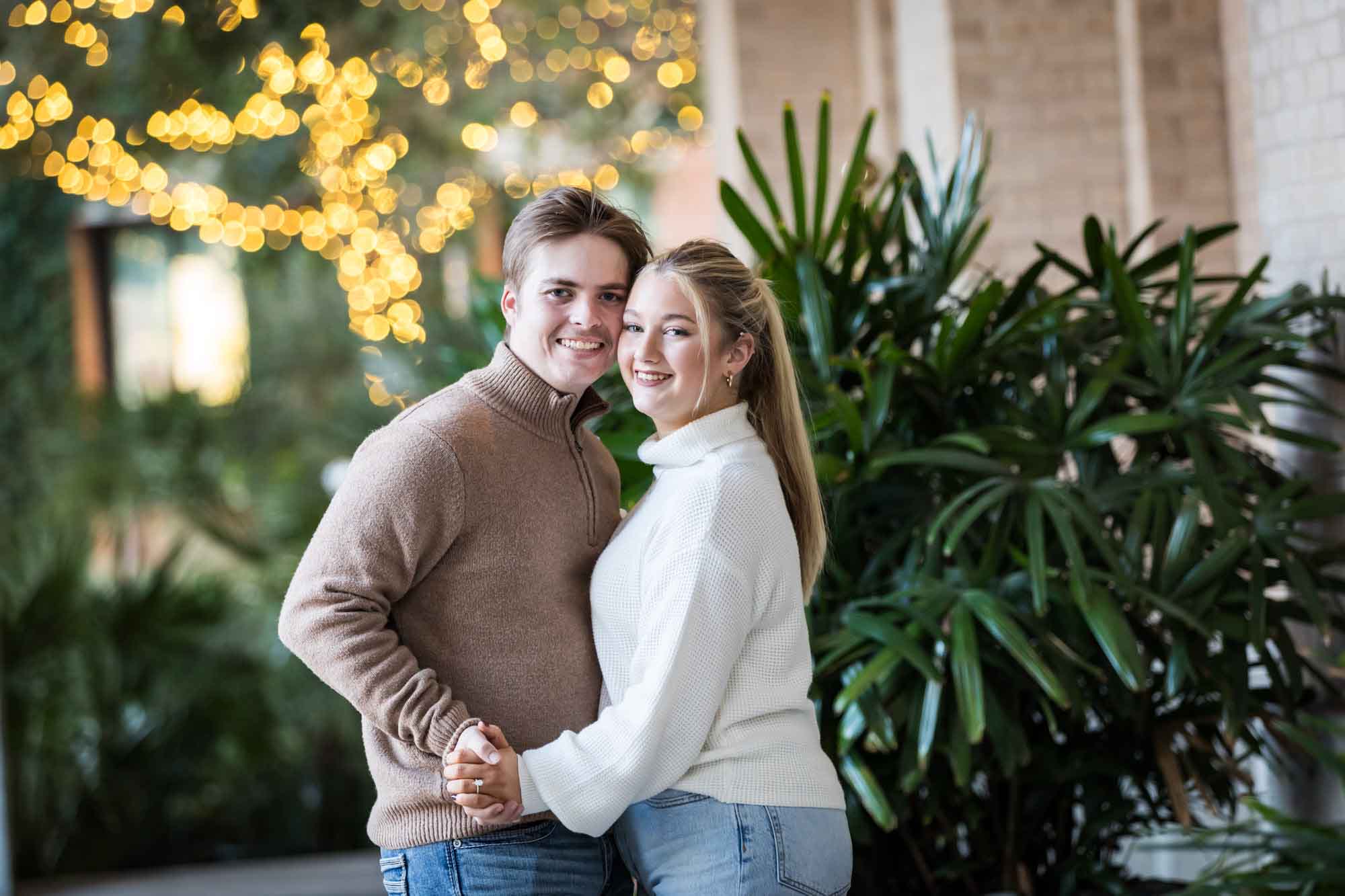 Couple wearing sweaters and dancing in front of string lights at the Pearl during an engagement photo shoot