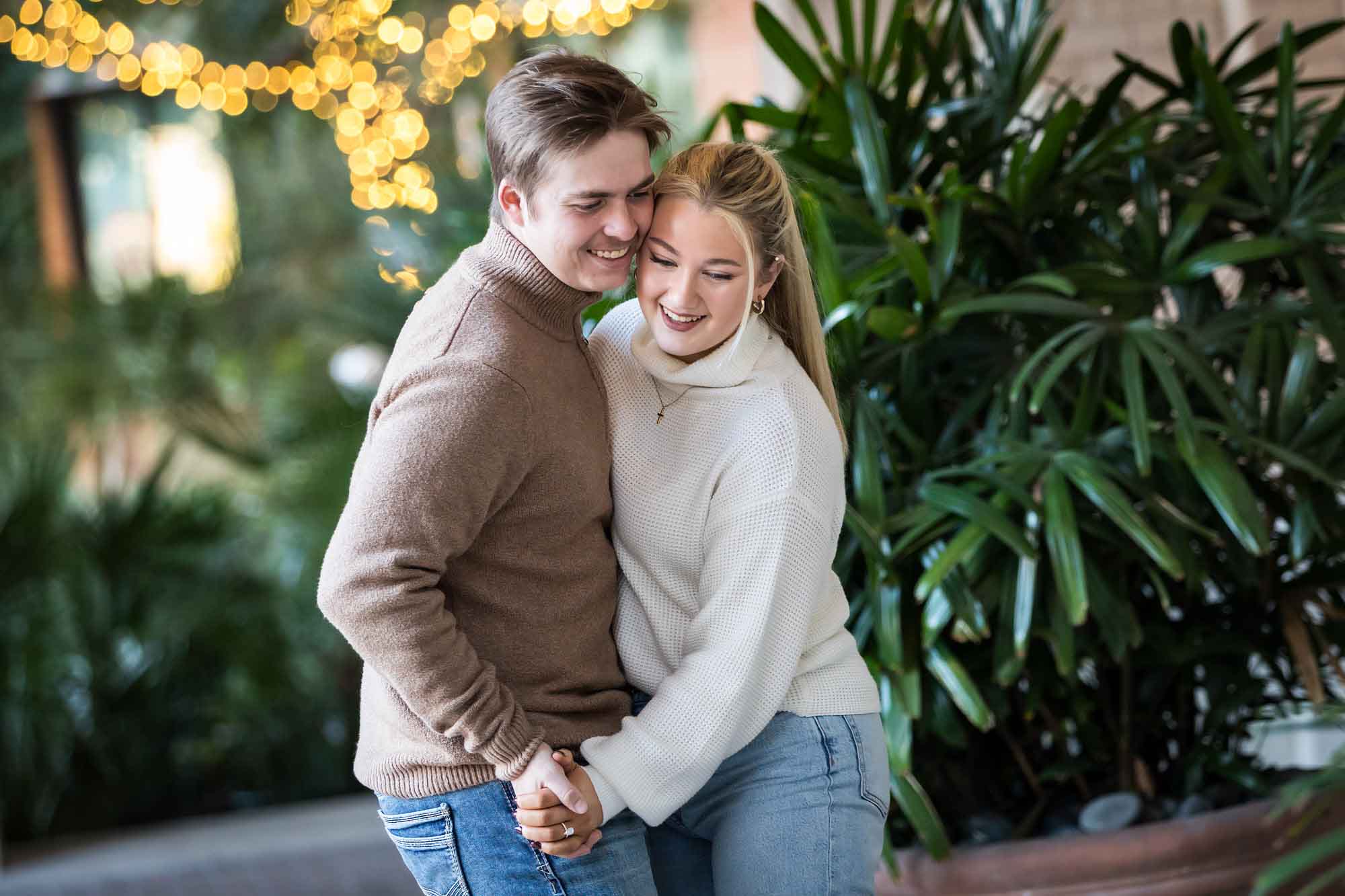 Couple wearing sweaters and dancing in front of string lights at the Pearl during an engagement photo shoot