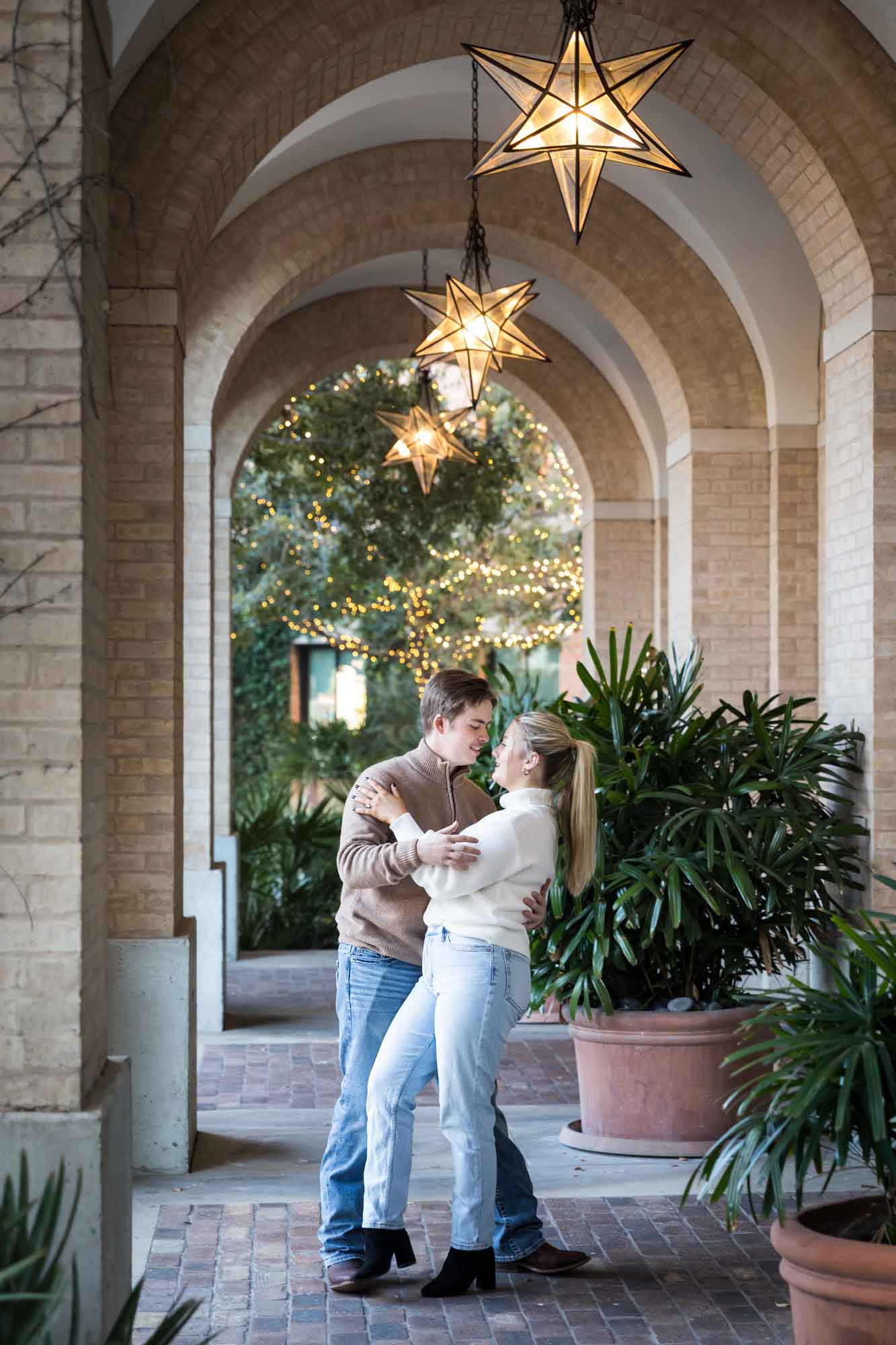 Couple wearing sweaters and dancing under brick arch with star lanterns at the Pearl during an engagement photo shoot