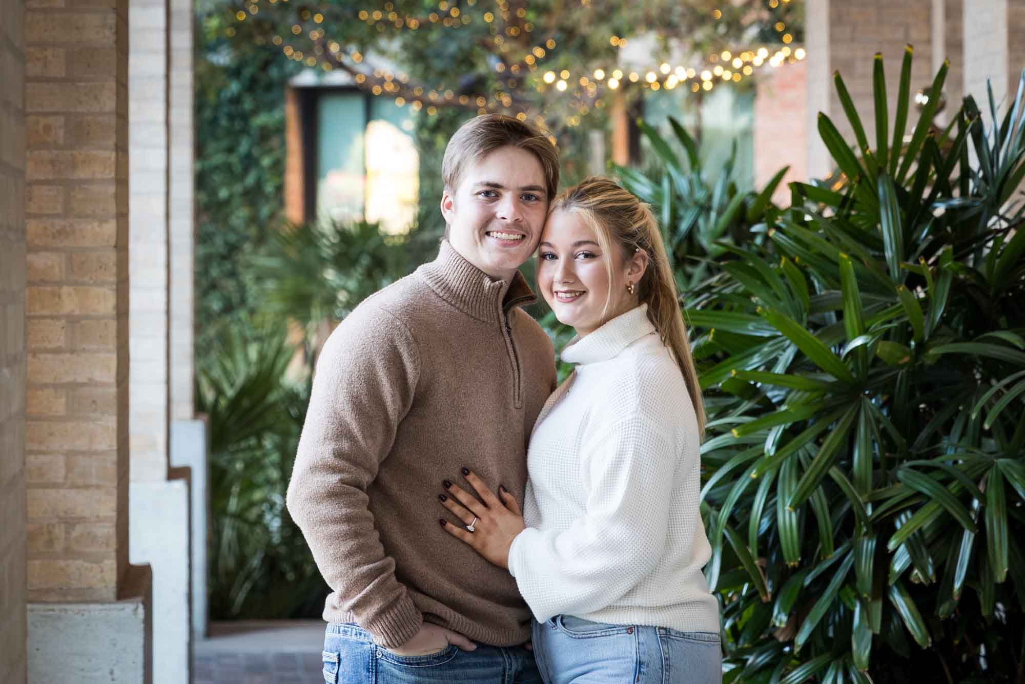 Couple wearing sweaters and hugging in front of string lights at the Pearl during an engagement photo shoot