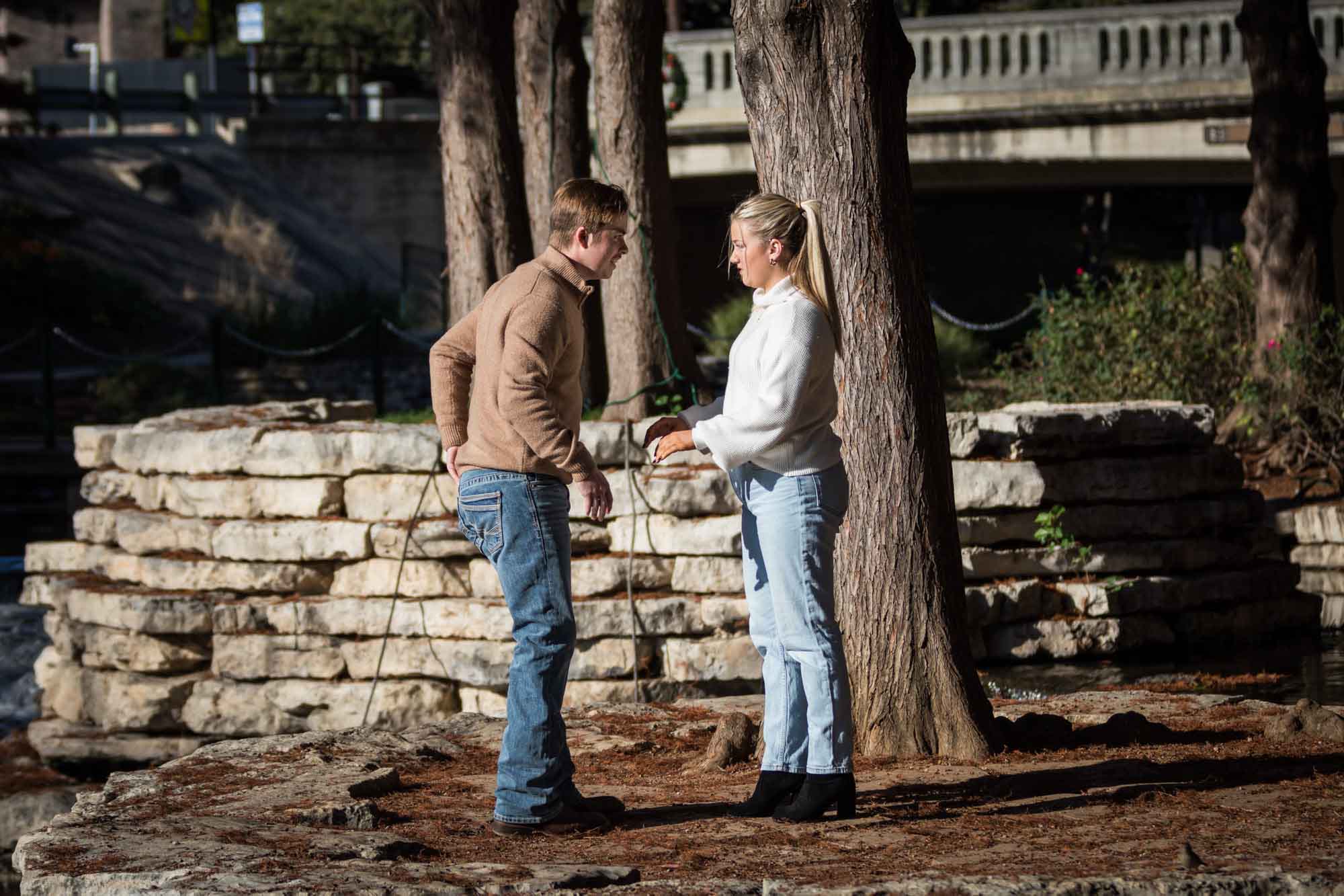 Man in white sweater pulling something out of pocket speaking to woman in white sweater for an article on the importance of timing for a surprise proposal